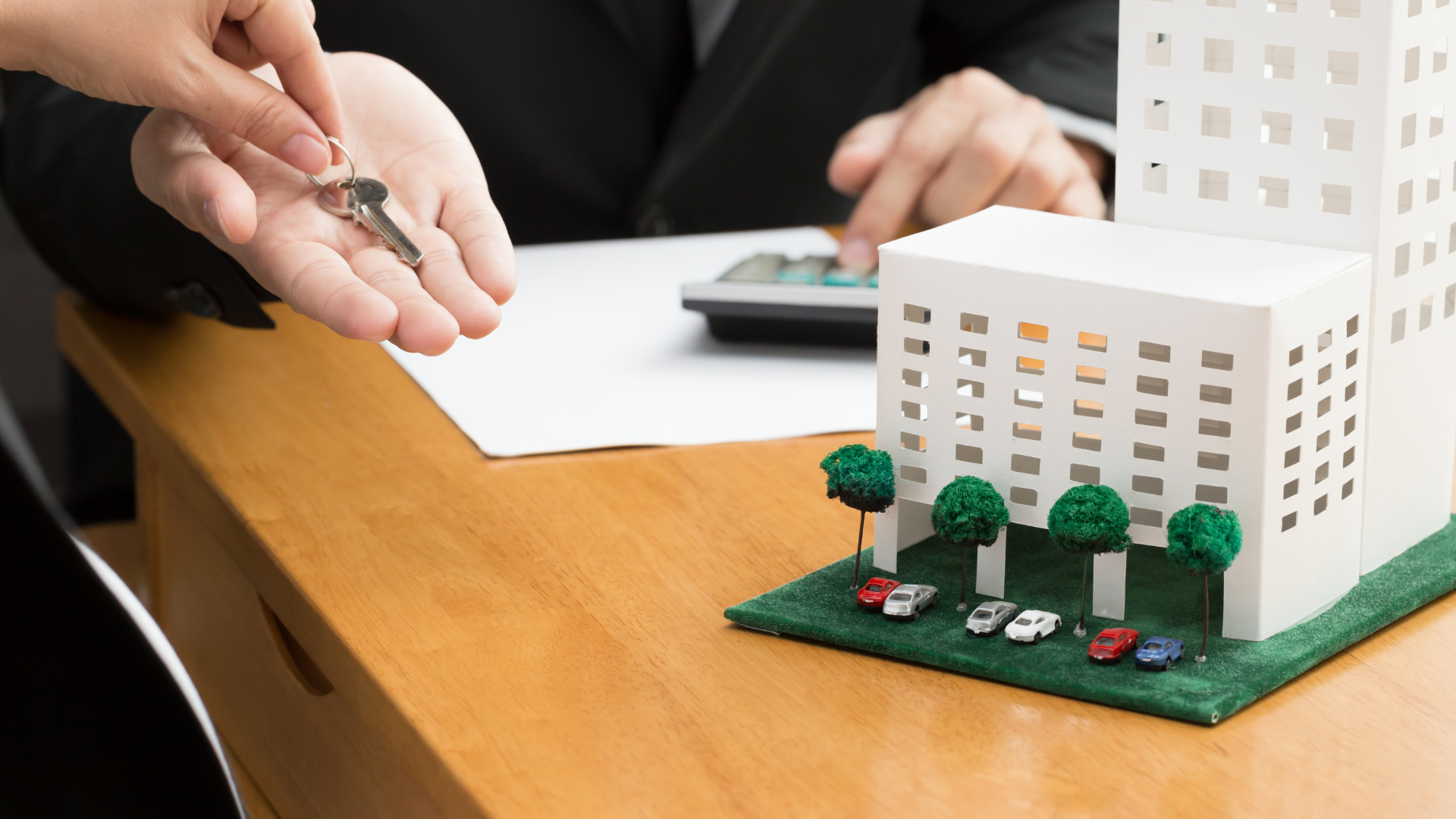 A person is giving a key to another person in front of a model of a building.