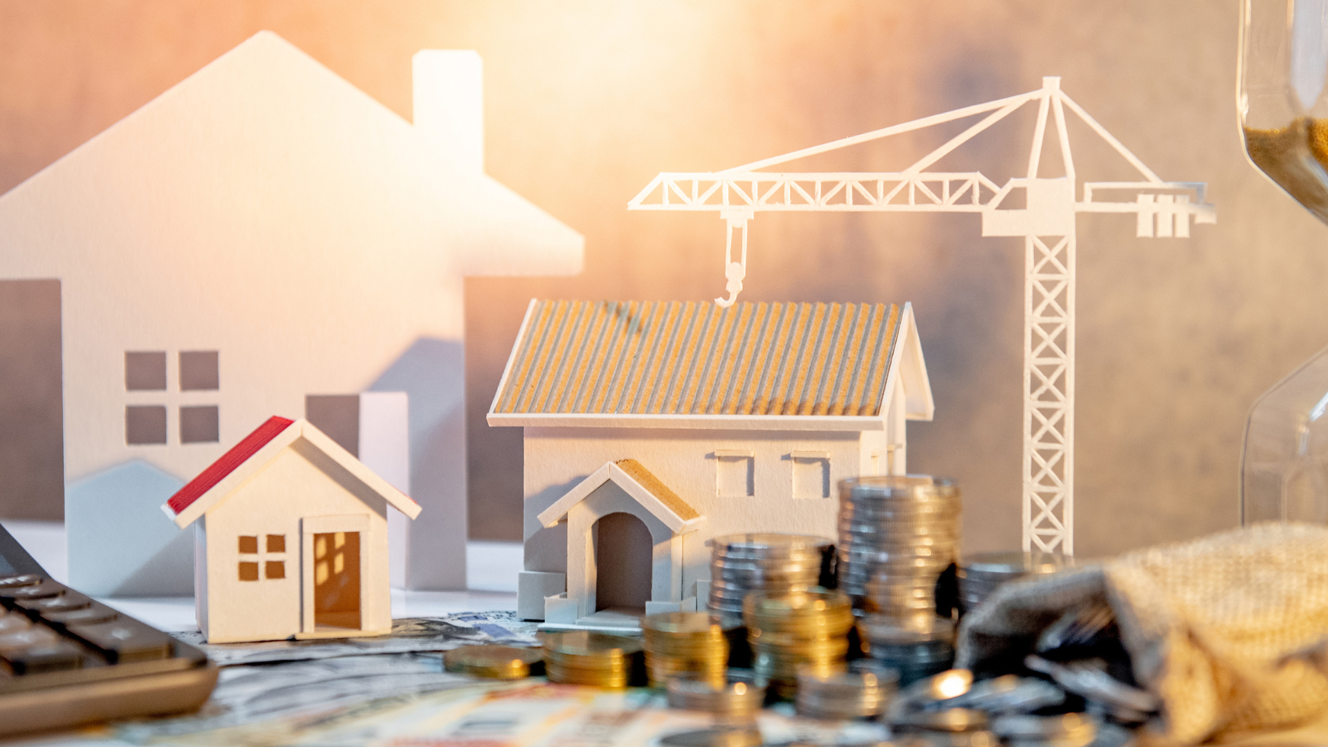 A stack of coins and a model house with a crane in the background.