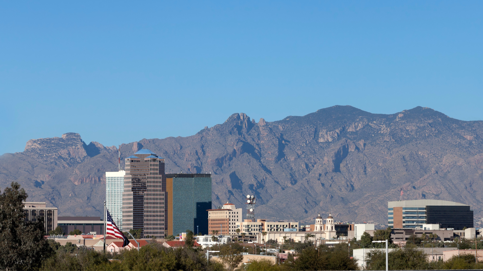 A city skyline with mountains in the background and a flag in the foreground.
