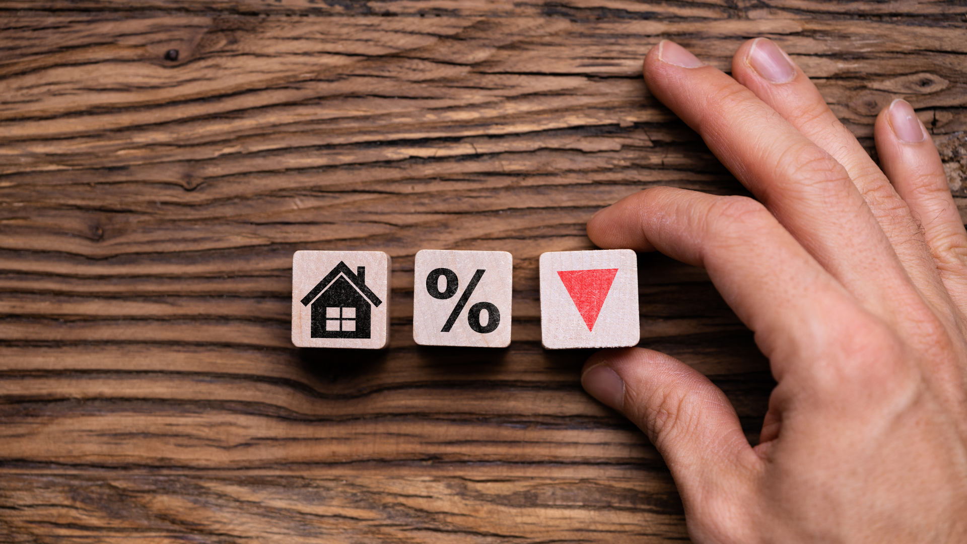 A person is holding a wooden block with a house , percent and arrow on it.