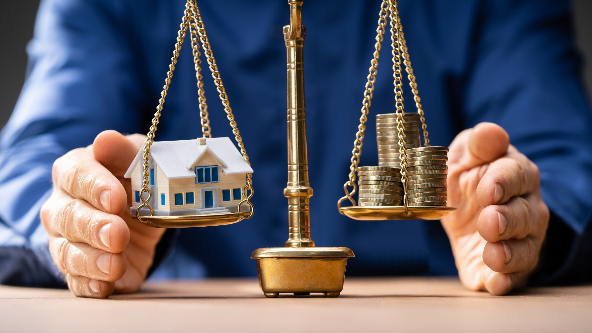 A person is holding a scale with a house and coins on it.
