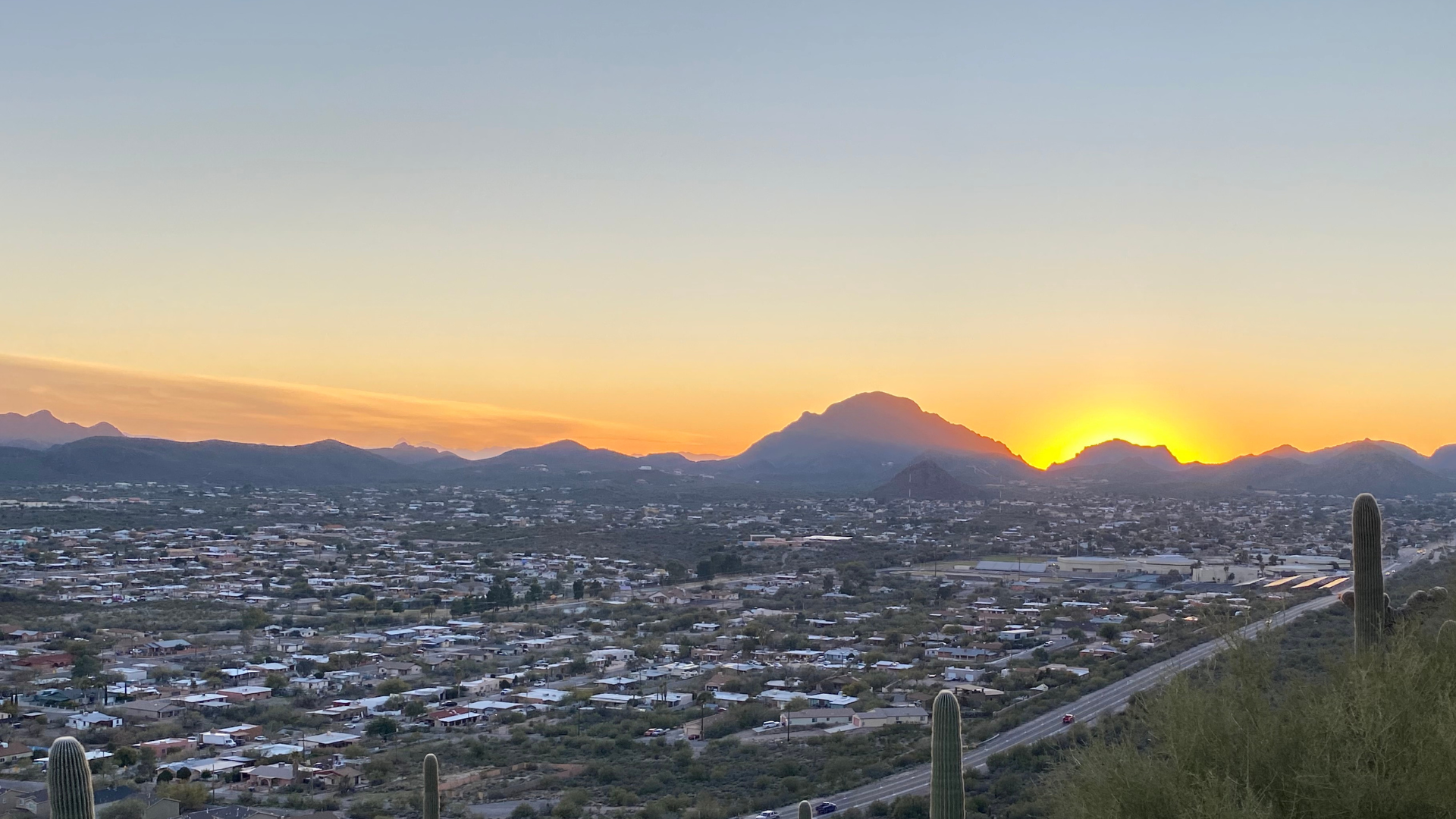 The sun is setting over a city with mountains in the background.