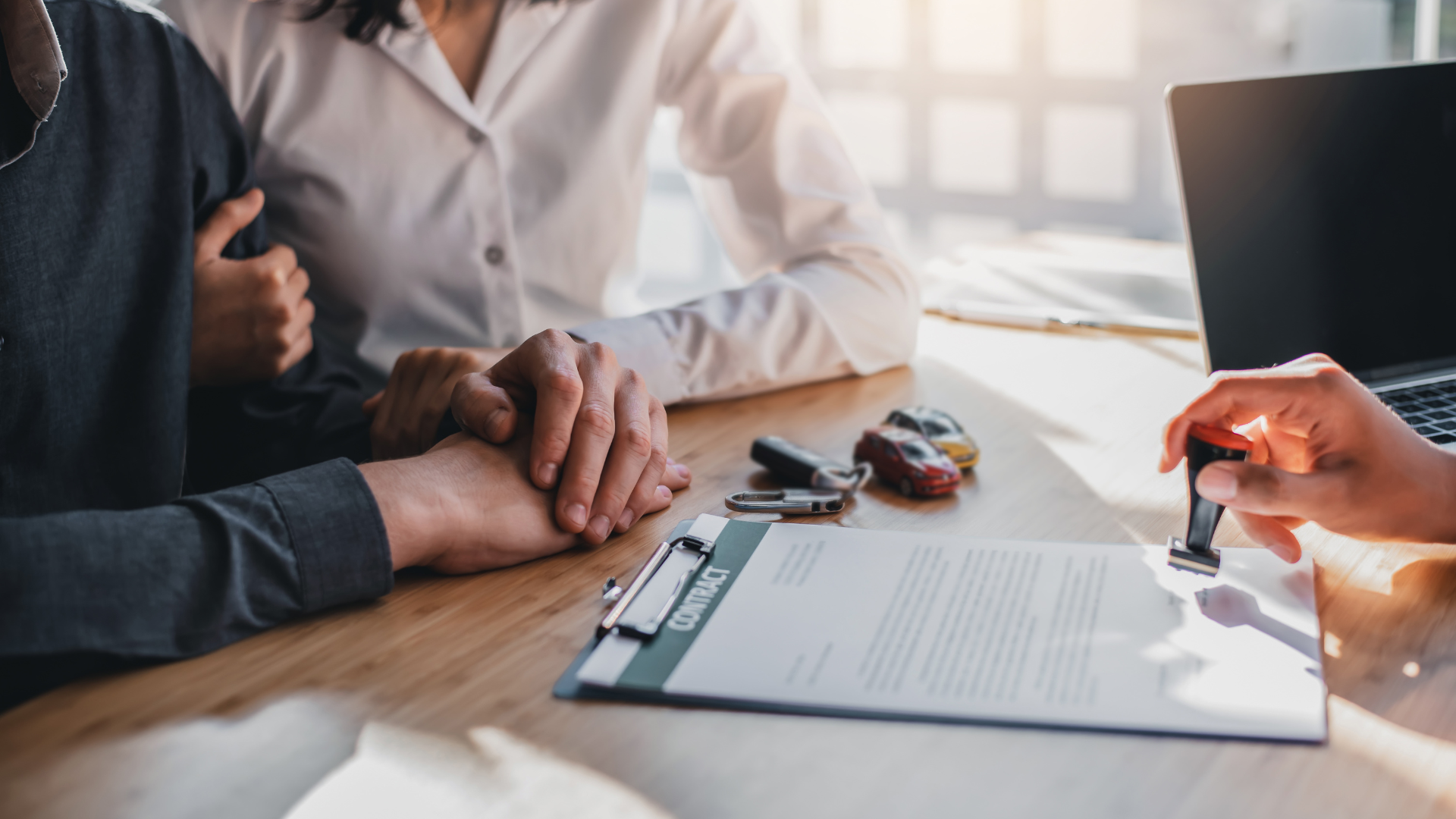A man and a woman are sitting at a table signing a car insurance agreement.
