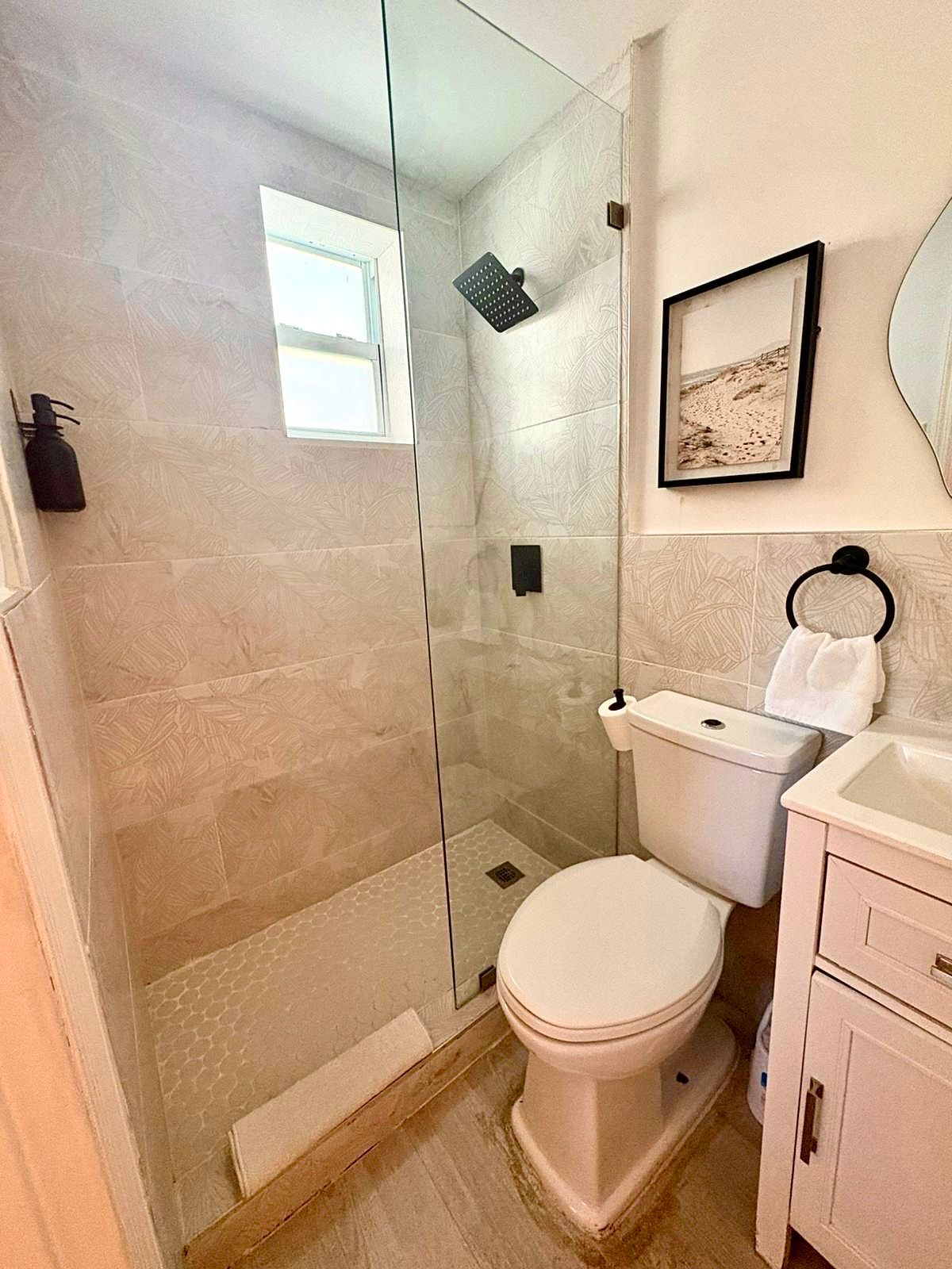 Small bathroom with beige tile, glass shower, toilet, and small sink.