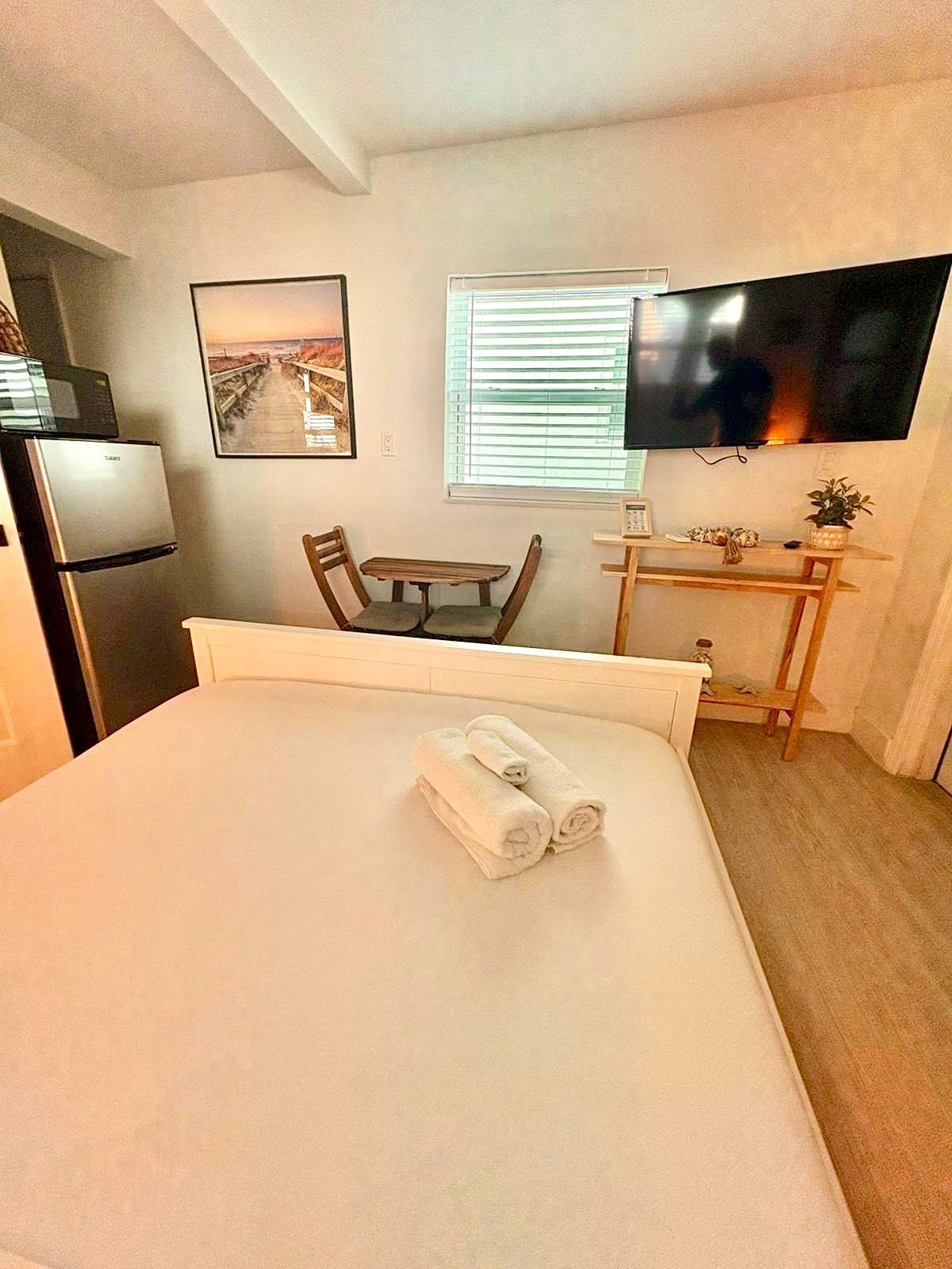 Small studio apartment with bed, TV, refrigerator, and small table.