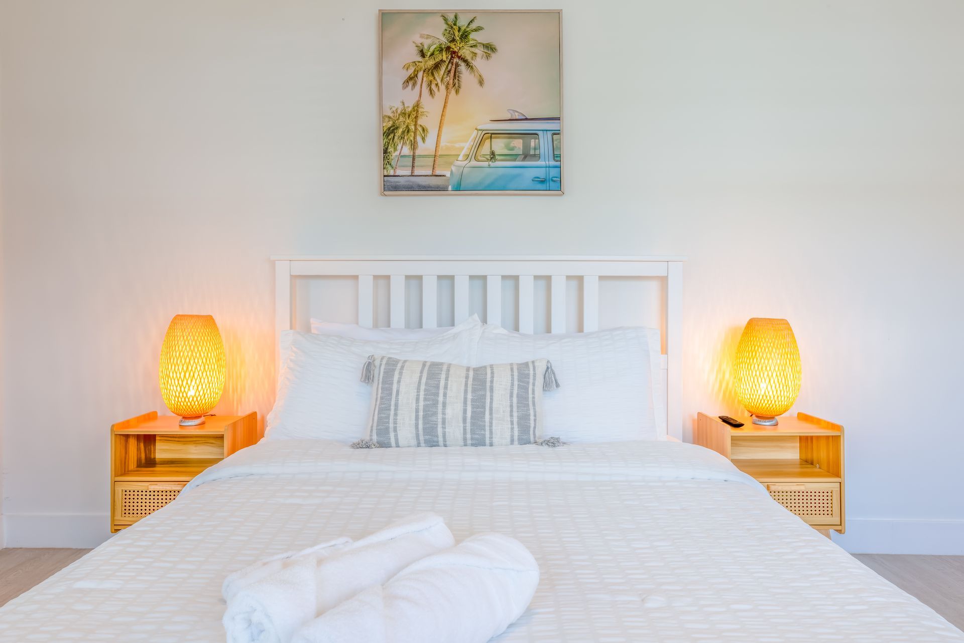 Bedroom with a white bed, nightstands, lamps, and beach-themed artwork.