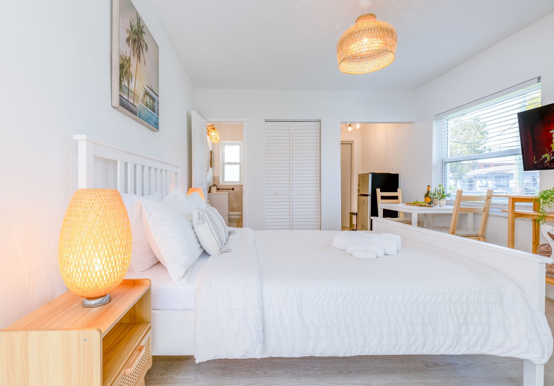White bedroom with bed, lamp, and table, near window.