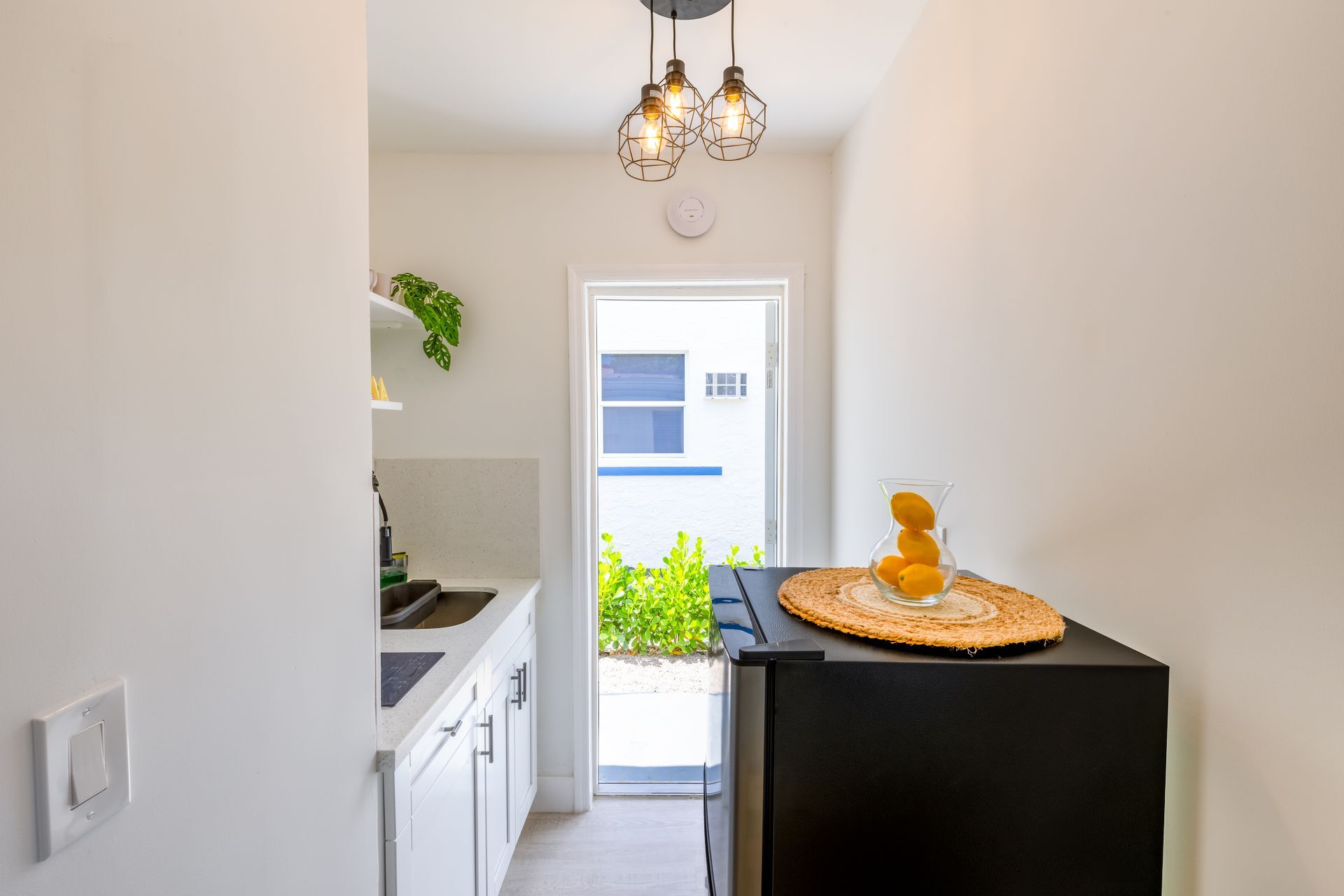 A small kitchen with a black refrigerator, white cabinets, and an open door to a yard.