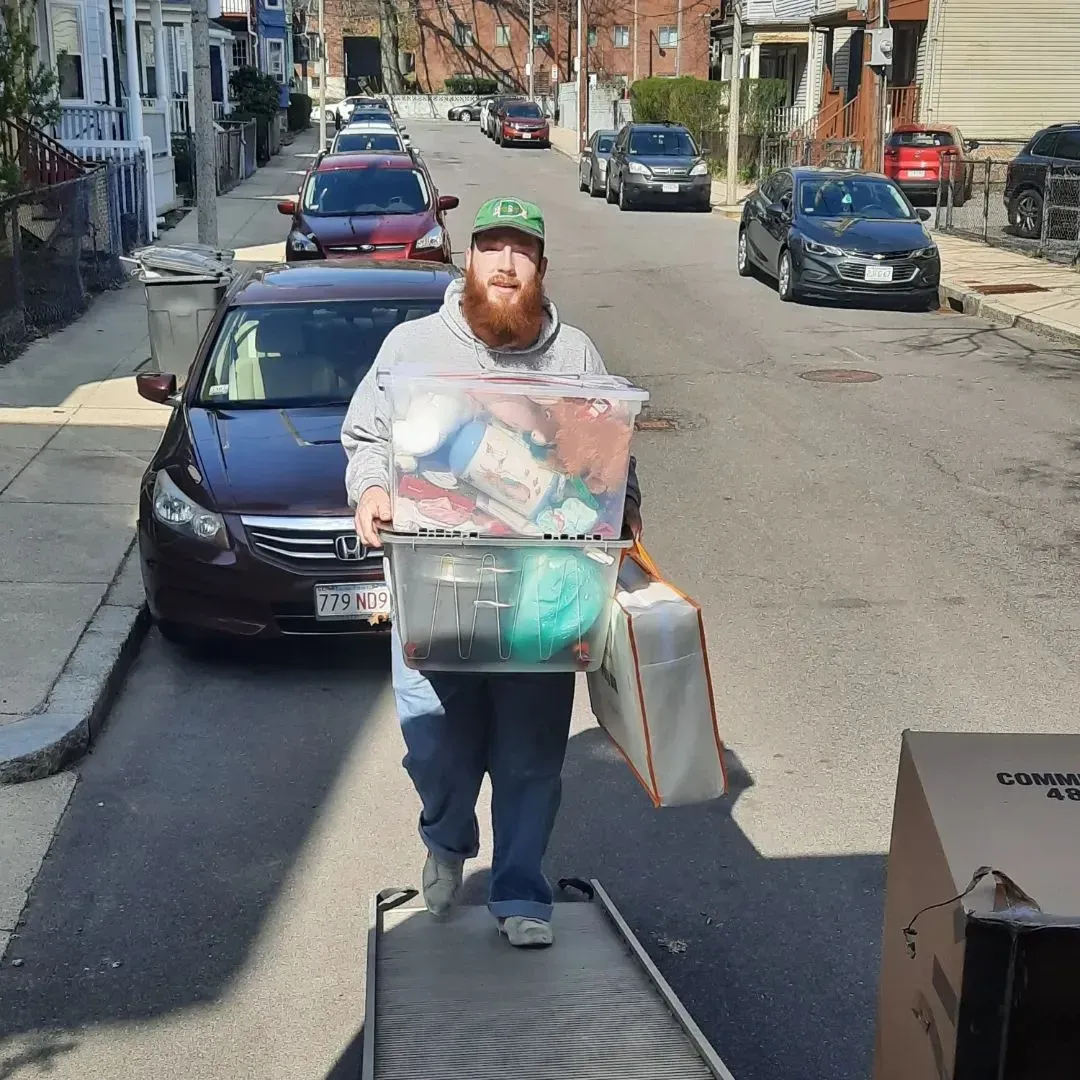 A man with a beard is carrying a large box down a street
