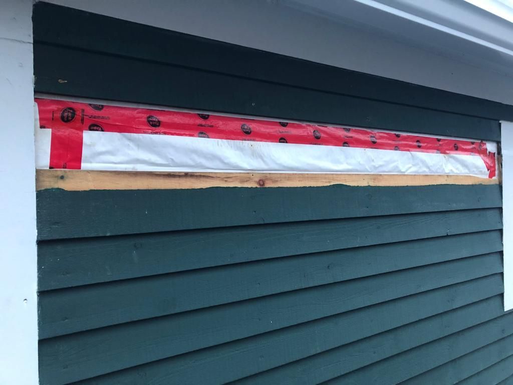 A green house with a window covered in red and white tape.