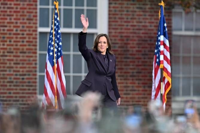 A woman in a suit is waving at a crowd in front of american flags. Angela Weiss/Getty Images