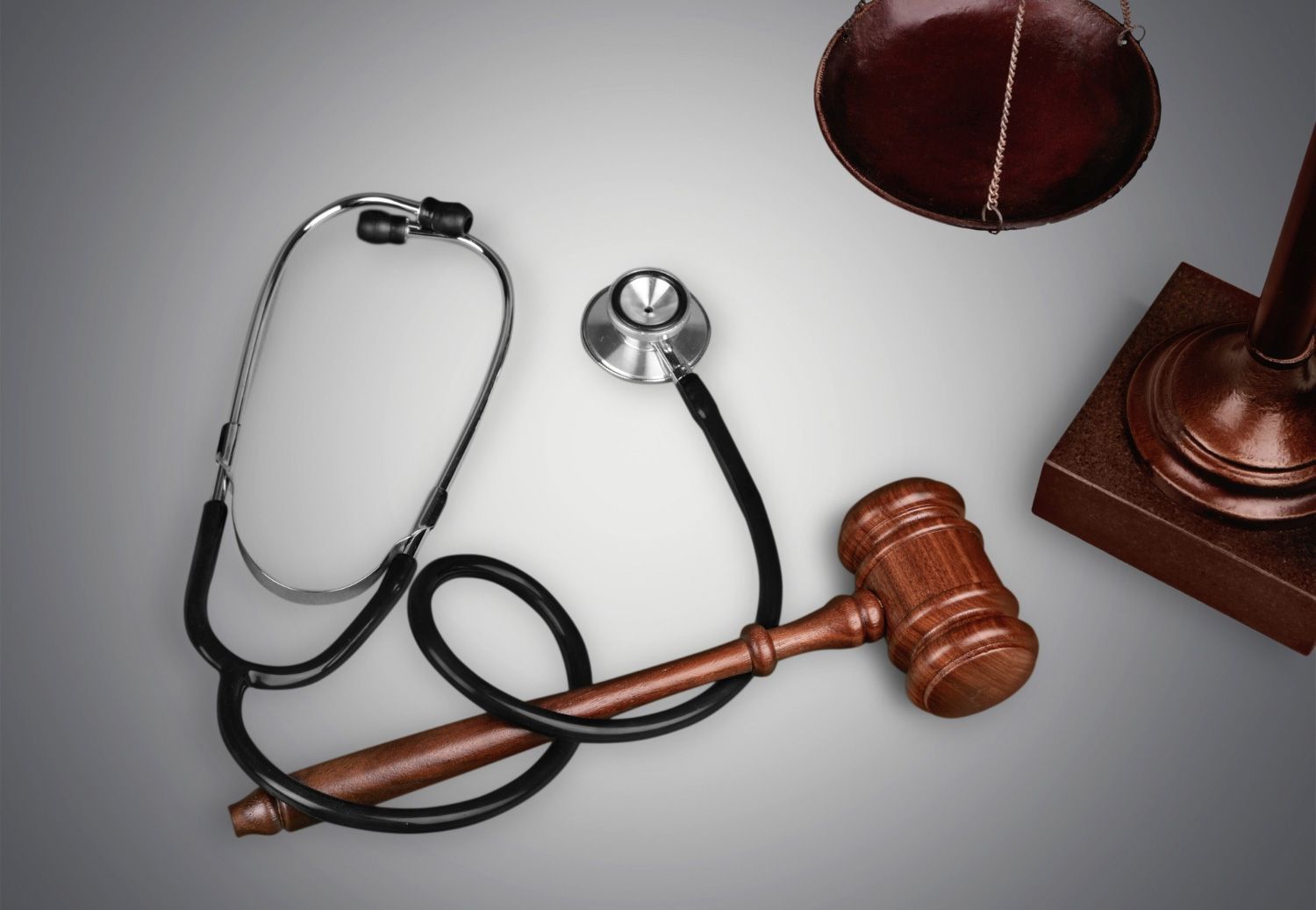 Stethoscope beside a wooden judge’s gavel and sounding block on a gray surface