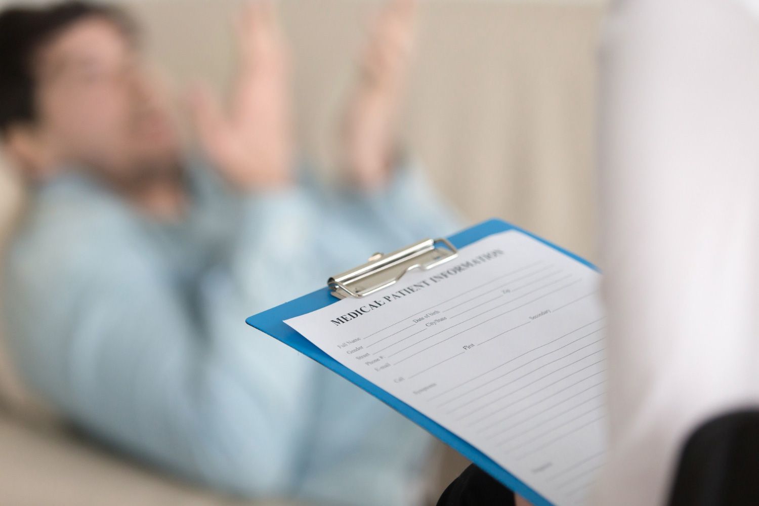 Clipboard with a blank form in foreground, blurred person sitting in the background with raised arms.