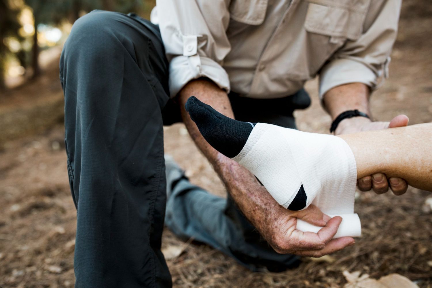 Person wrapping a white bandage around another person's ankle outdoors