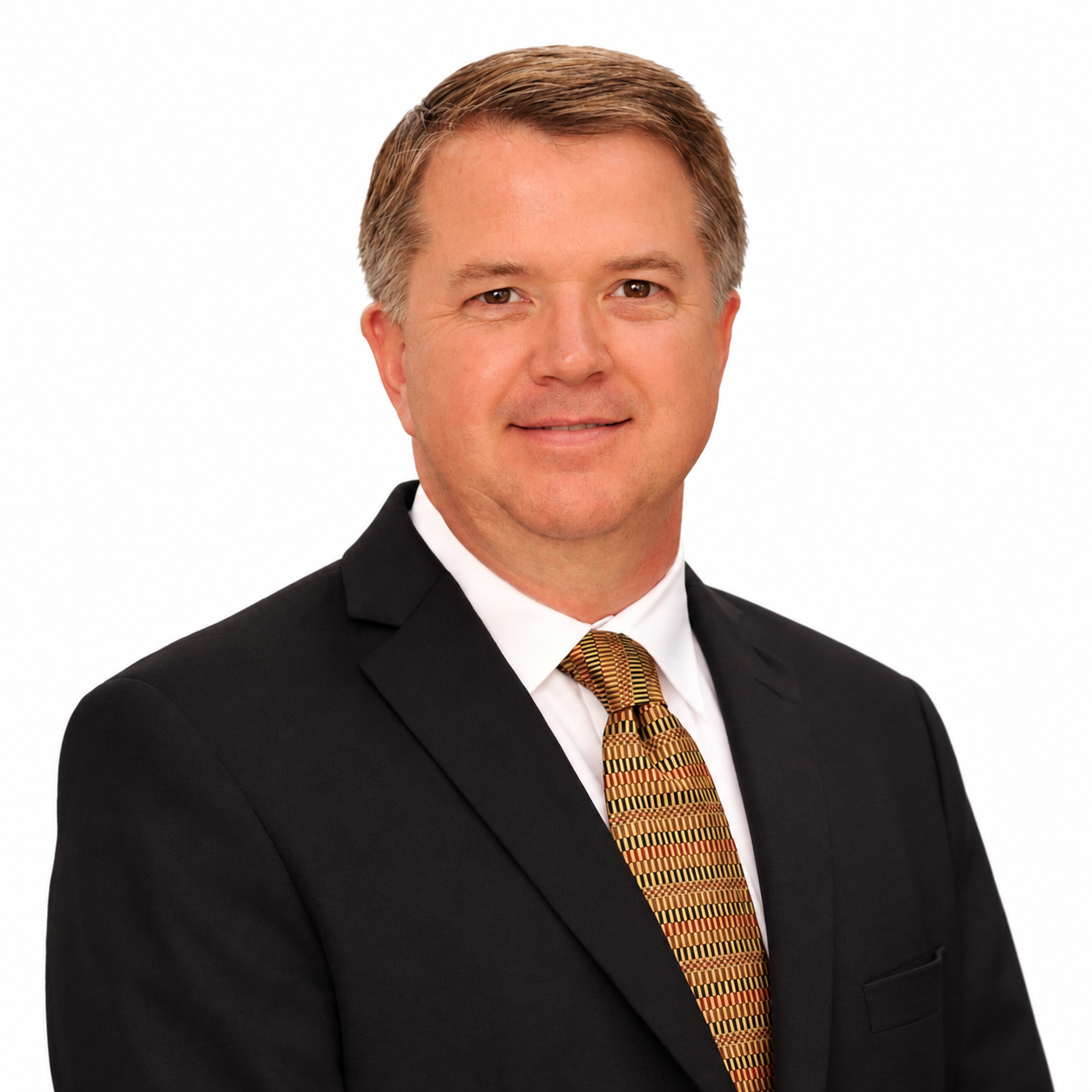 Professional headshot of a man in a black suit, white shirt, and patterned tie on a white background