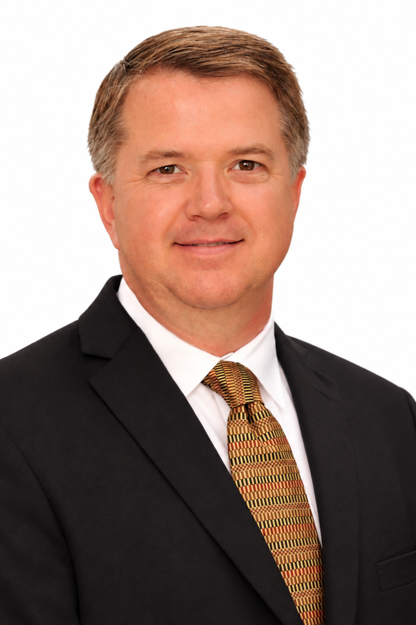 Portrait of a man in a black suit, white shirt, and patterned tie against a white background