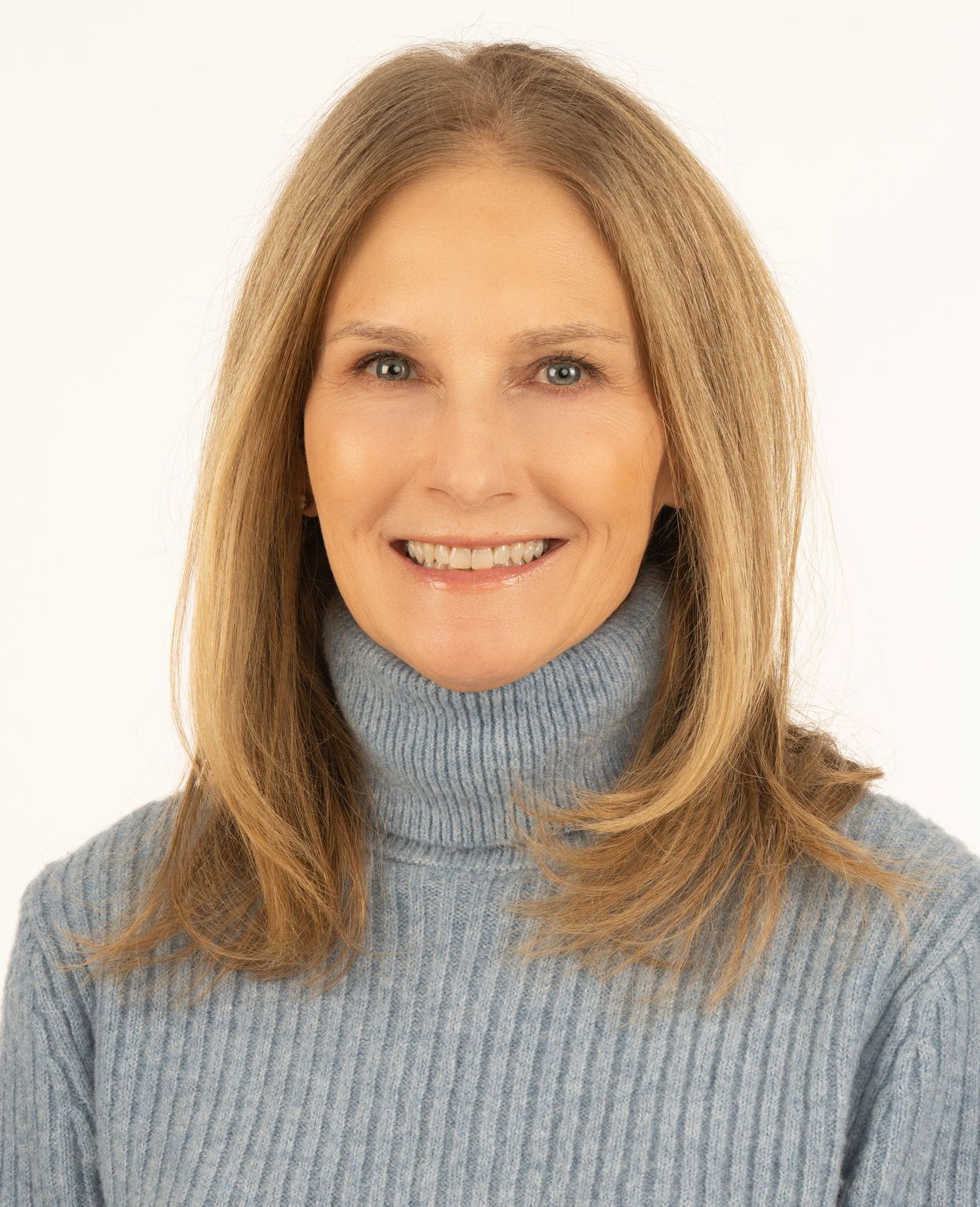 Studio portrait of a smiling person with long light brown hair wearing a blue turtleneck sweater.