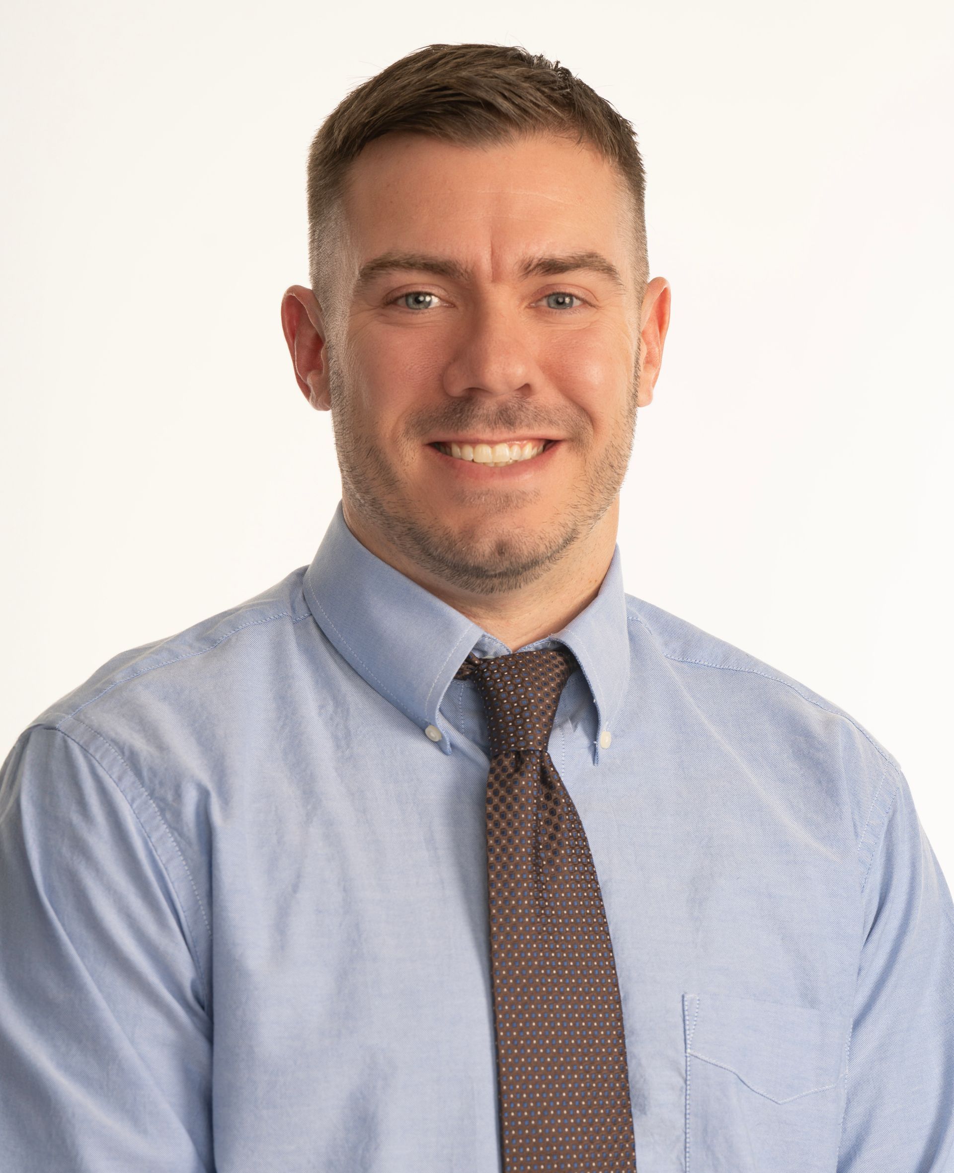 Smiling person in a light blue shirt and brown tie against a white background