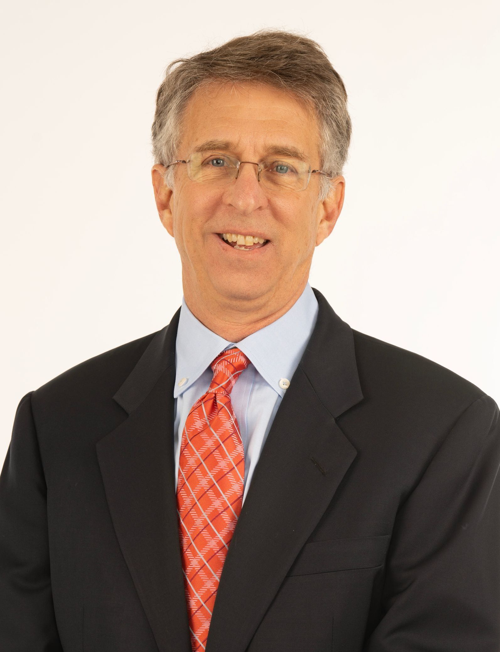 Man in dark suit and red tie smiling against a plain white background