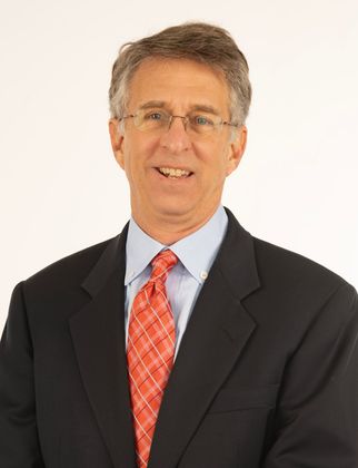 Portrait of a man in a dark suit, light blue shirt, and red patterned tie against a white background