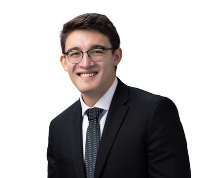 Smiling person in a black suit, white shirt, and patterned tie against a white background
