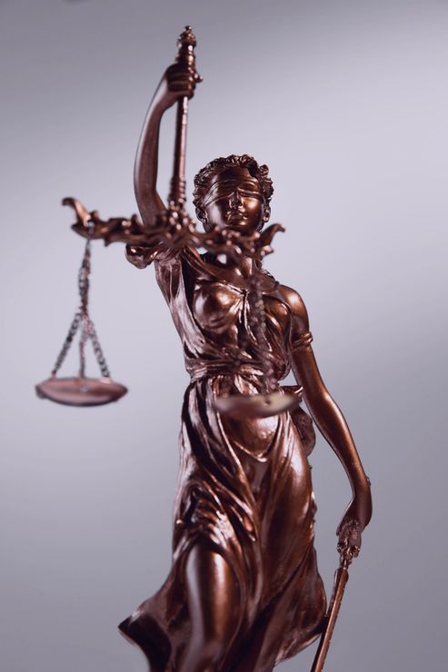 Bronze Lady Justice statue holding scales, with raised sword, against a gray background