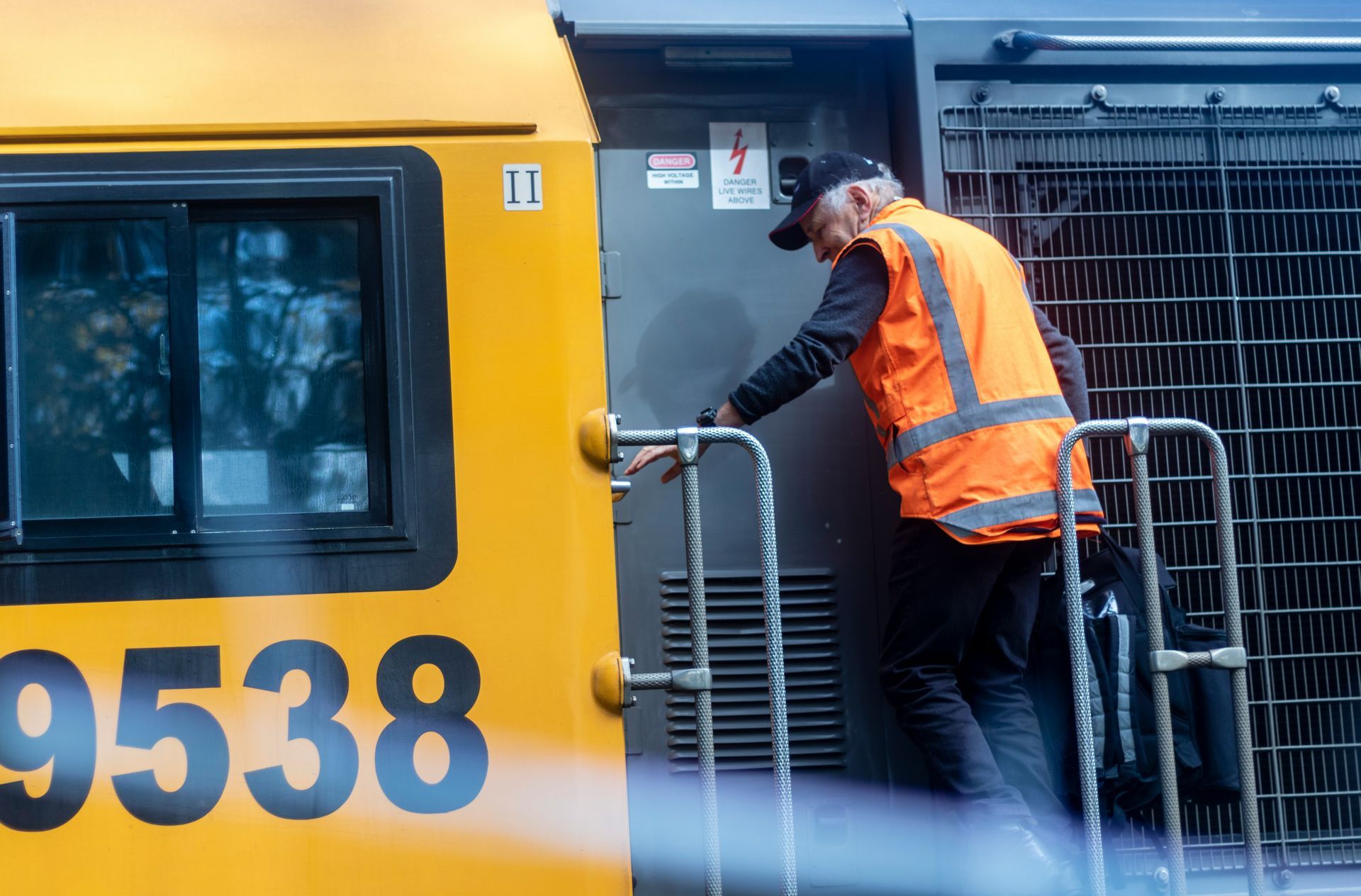 Worker in orange safety vest cleaning a yellow train beside a platform barrier