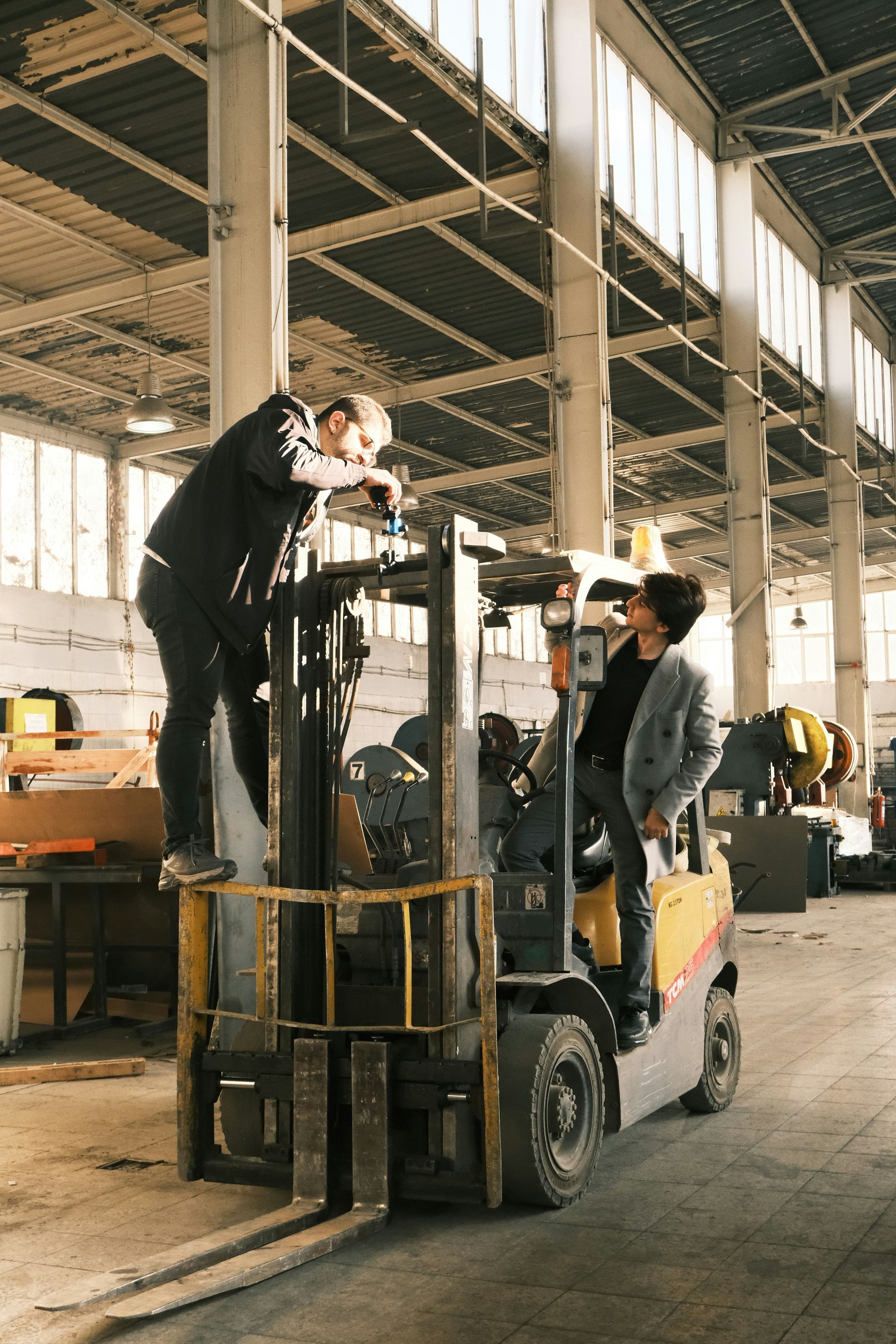 Two workers atop a forklift stacking materials in a warehouse.