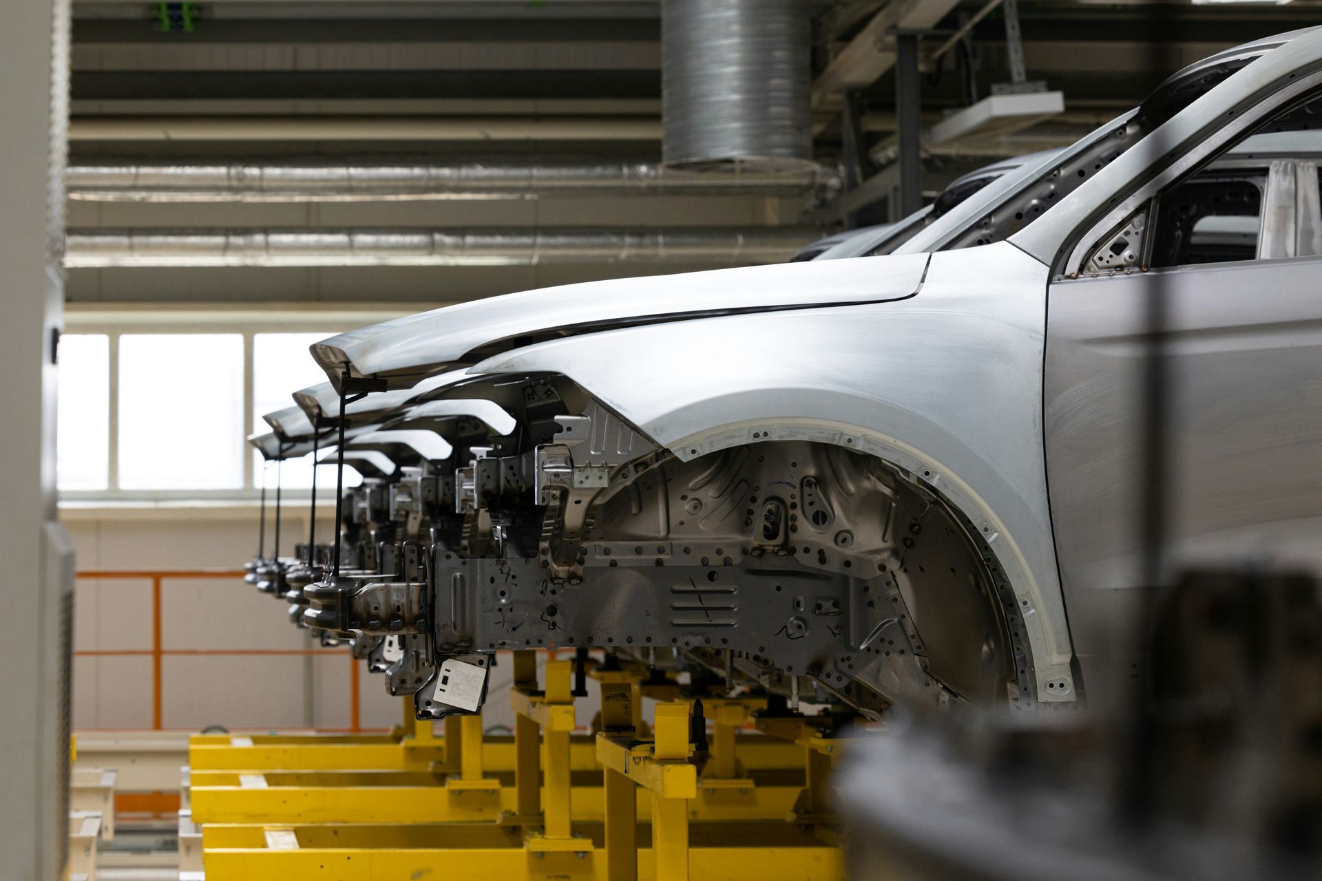 Silver car body in an assembly line, front end mounted on yellow factory supports