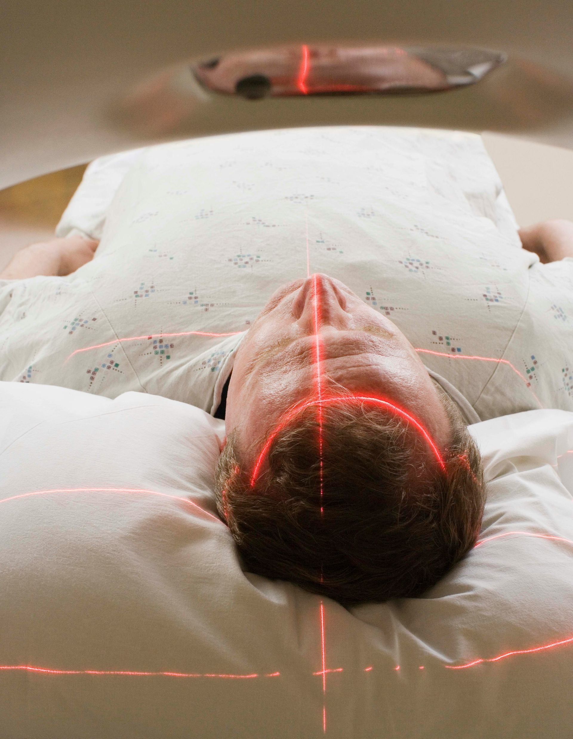 Person lying on a table under a medical scan, with red laser lines across the body.