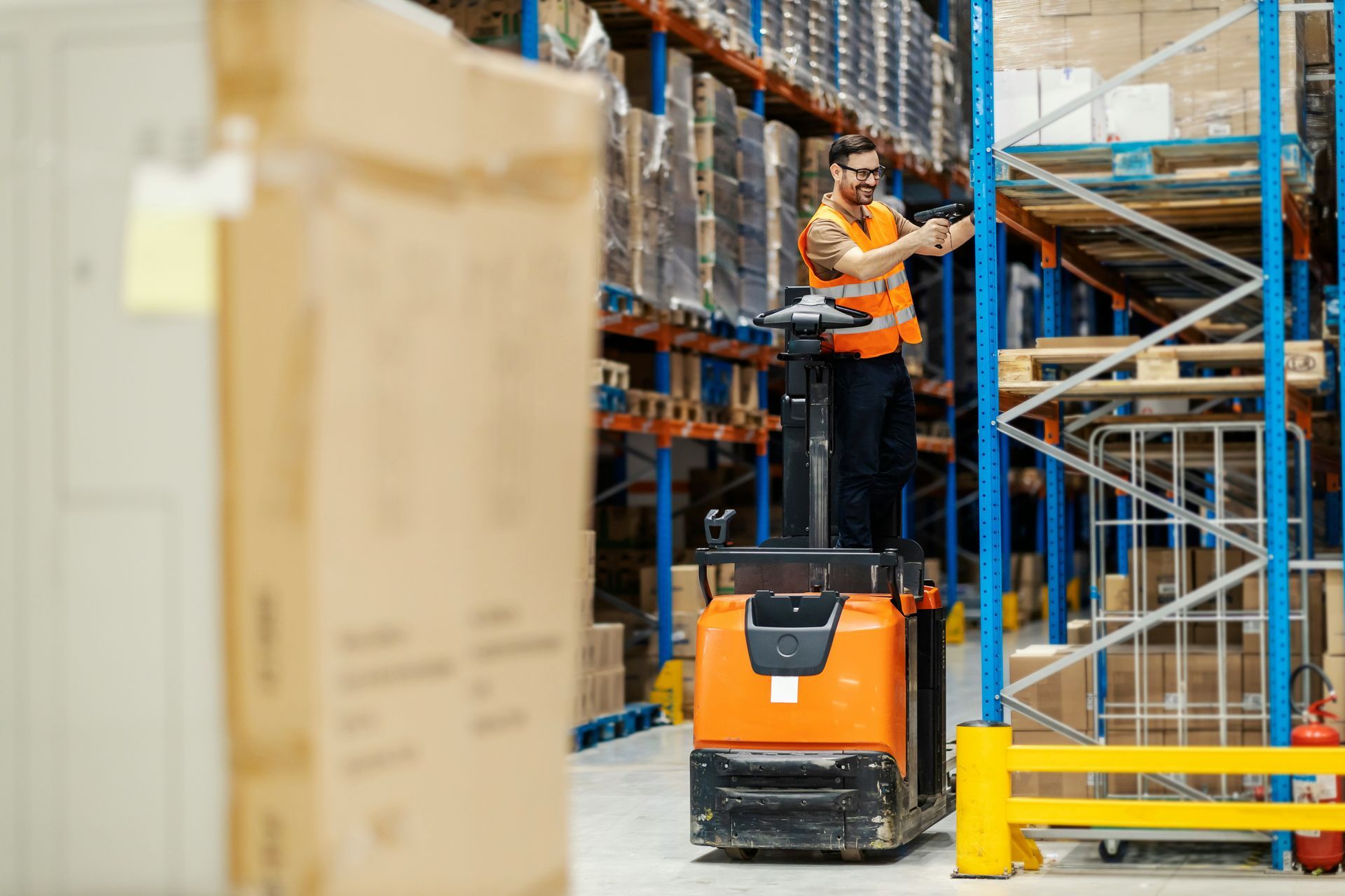 Worker on an orange forklift in a warehouse reaching for boxes on high shelves