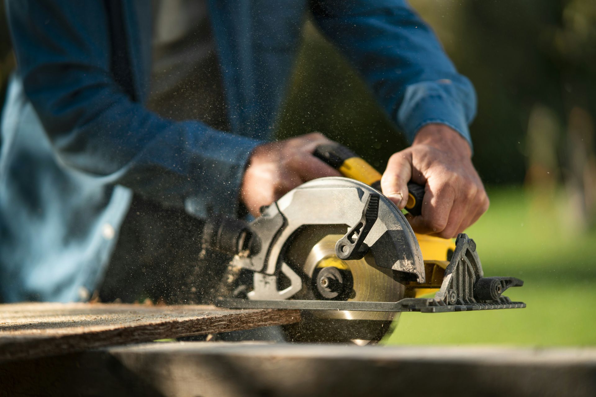 Person using a yellow circular saw to cut a wooden board outdoors.