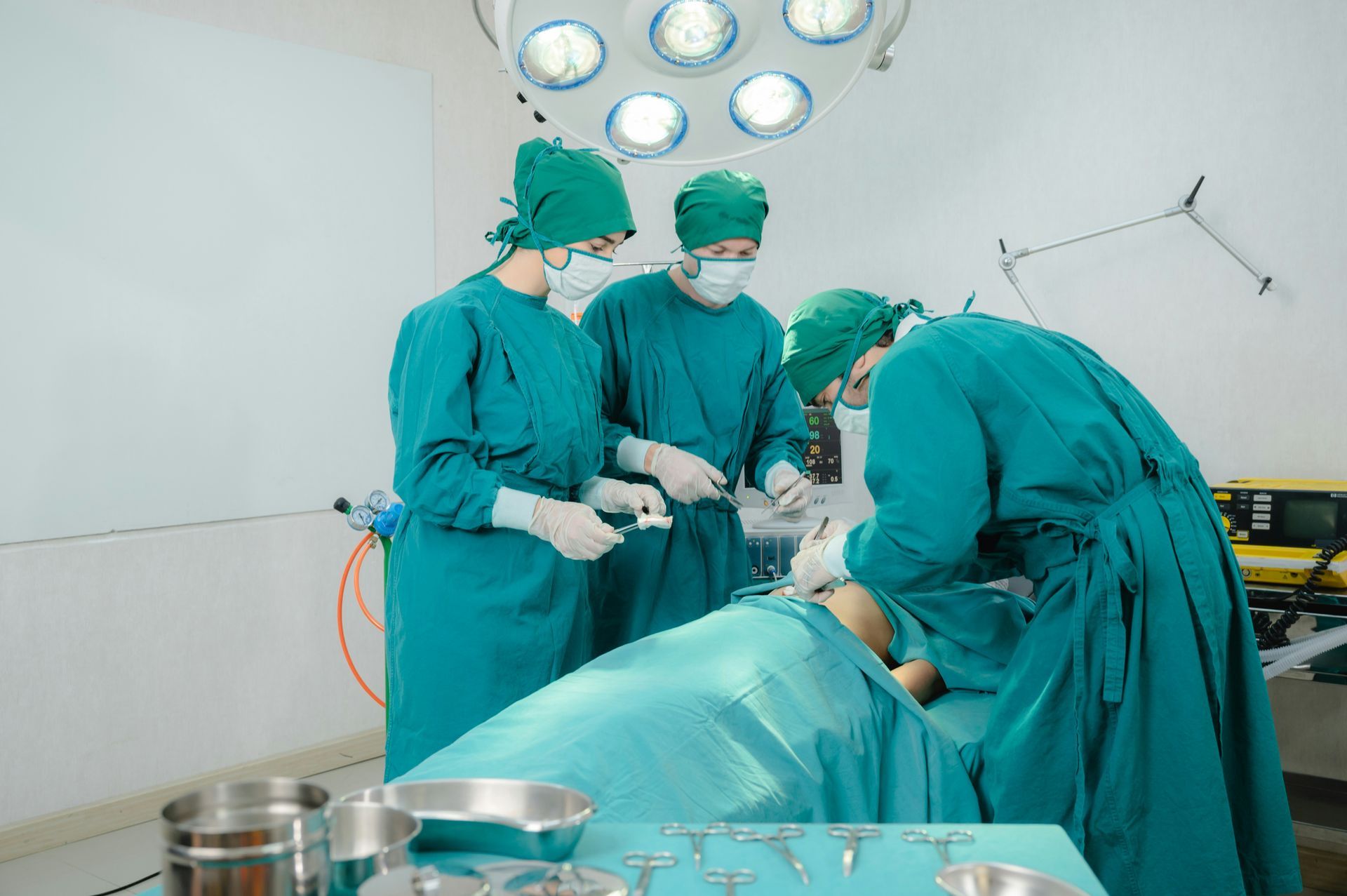 Surgeons in green scrubs performing an operation in an operating room under bright surgical lights