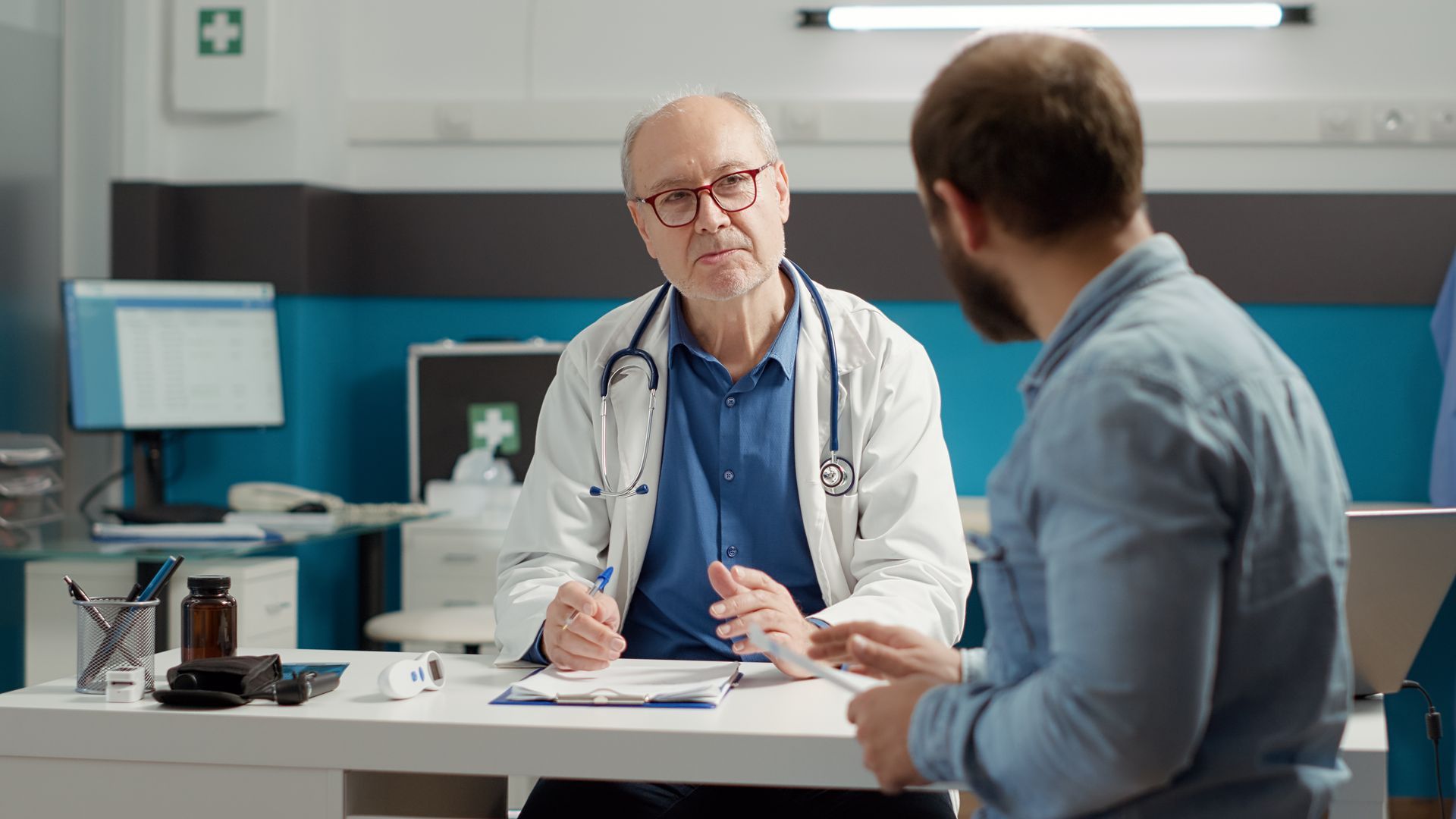 Doctor talking with a patient in a clinic office, with a desk and computer in the background