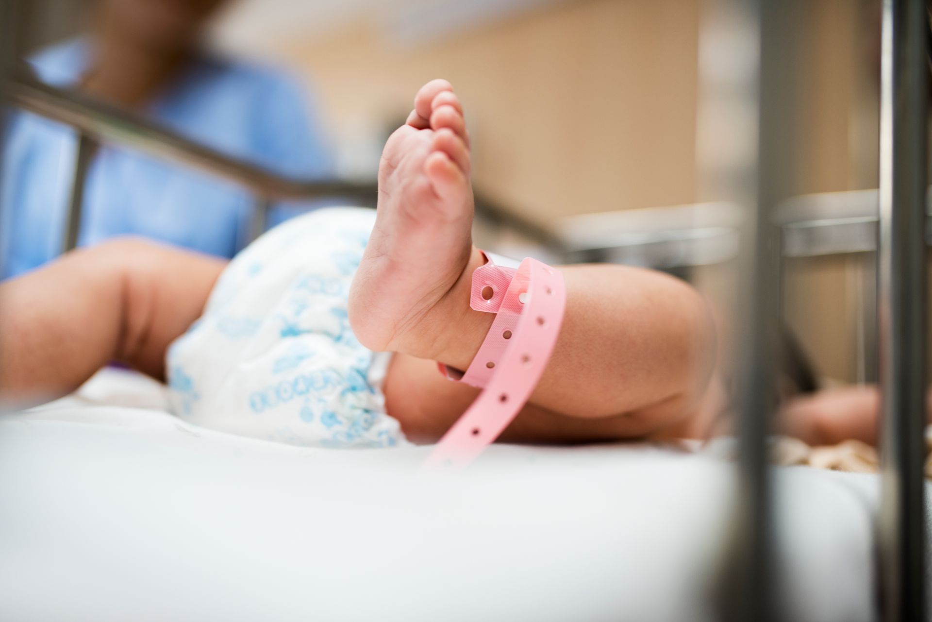 Baby in a diaper with a pink hospital wristband, lying in a hospital crib