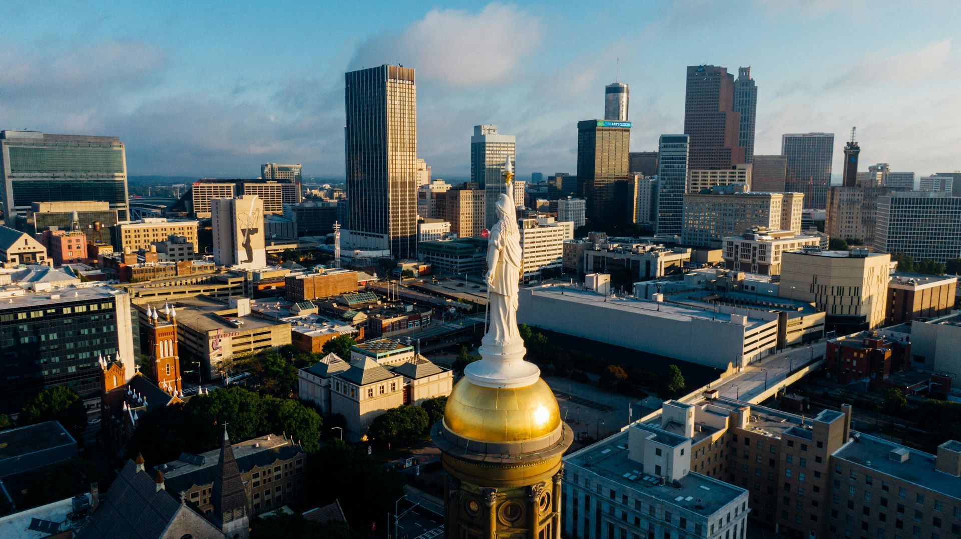 Aerial city skyline with a golden dome and white statue in the foreground at sunset