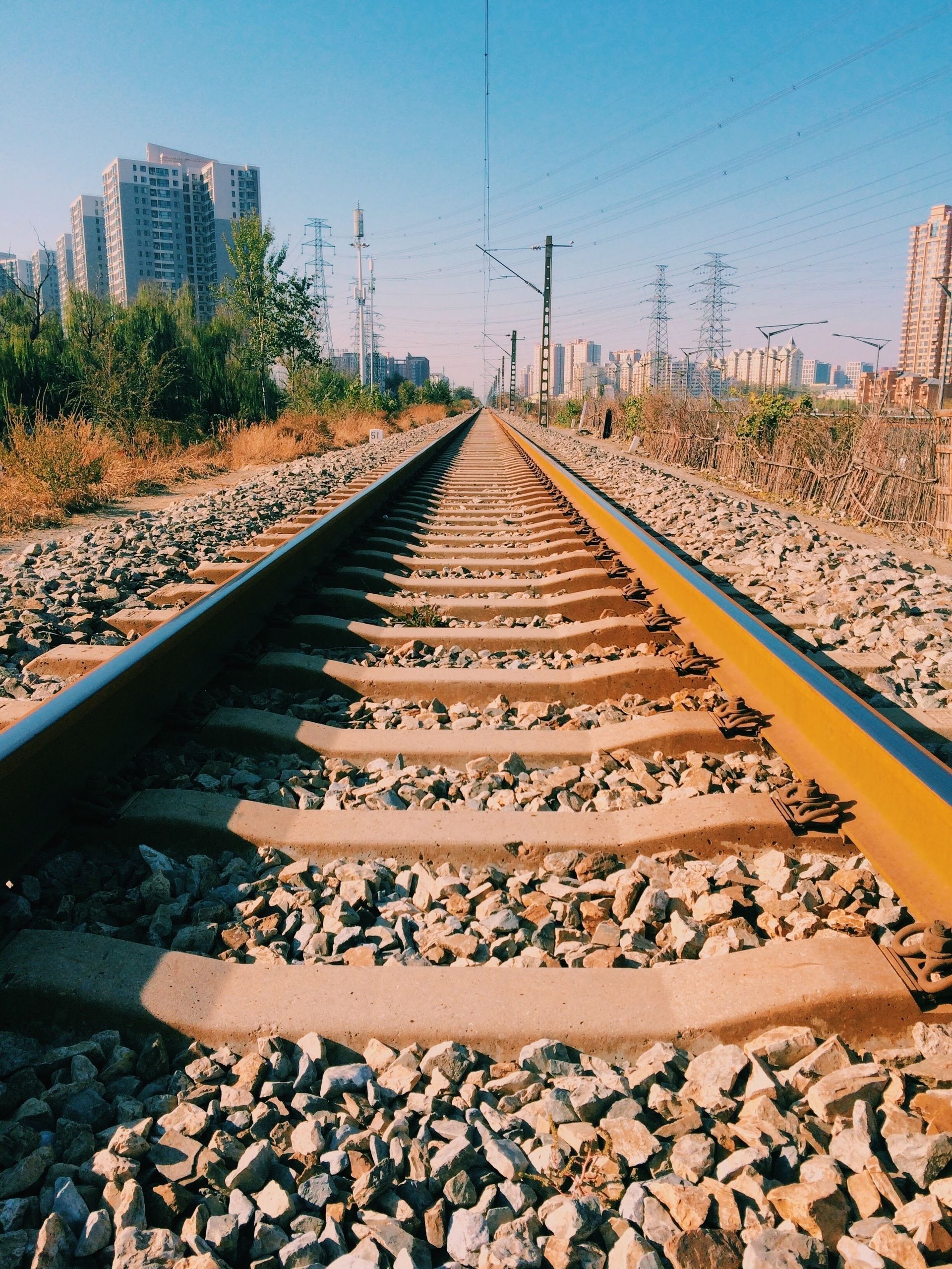 Railroad tracks stretching into the distance through a dry, sunlit urban landscape.