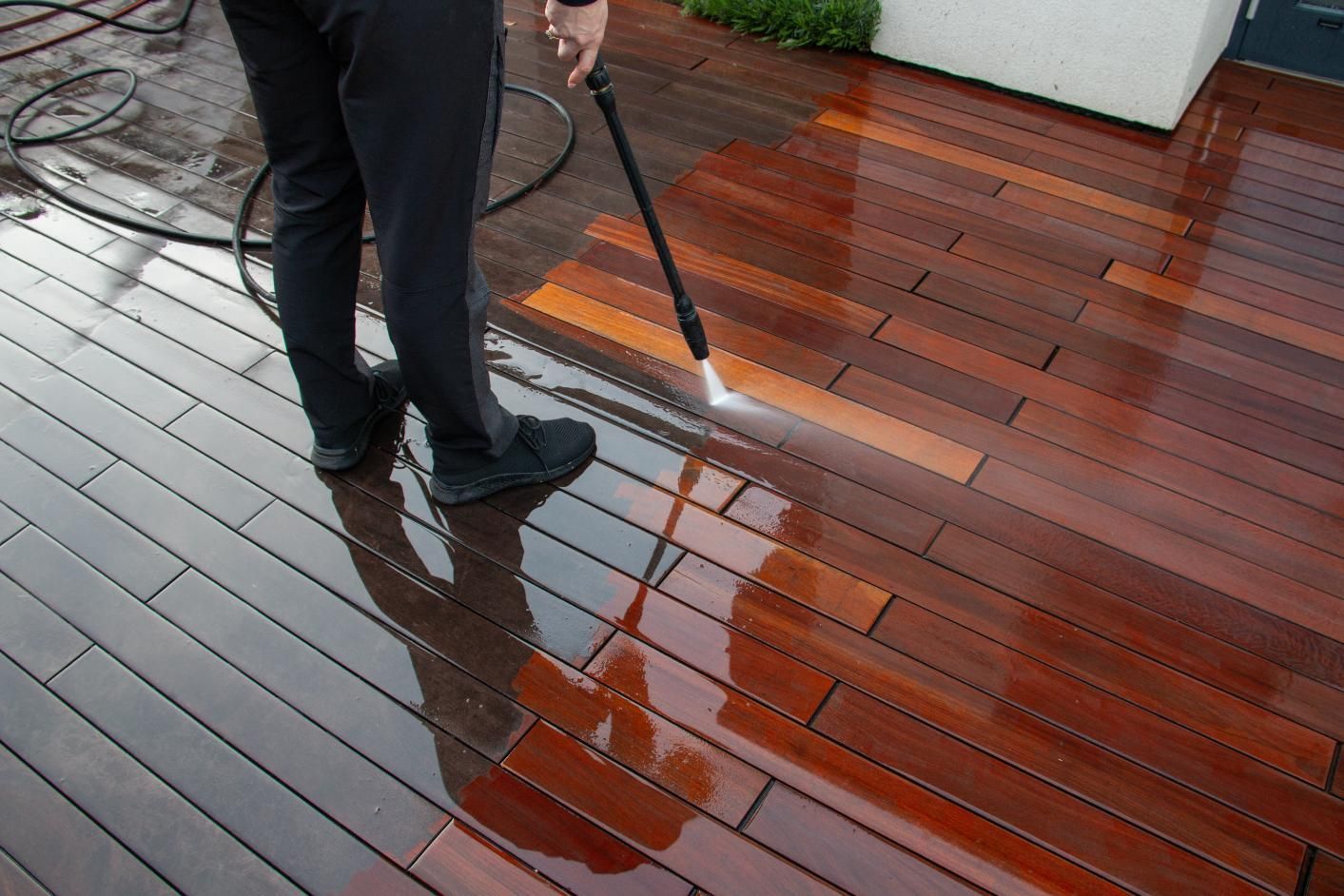 Person pressure-washing a wet wooden deck on a patio