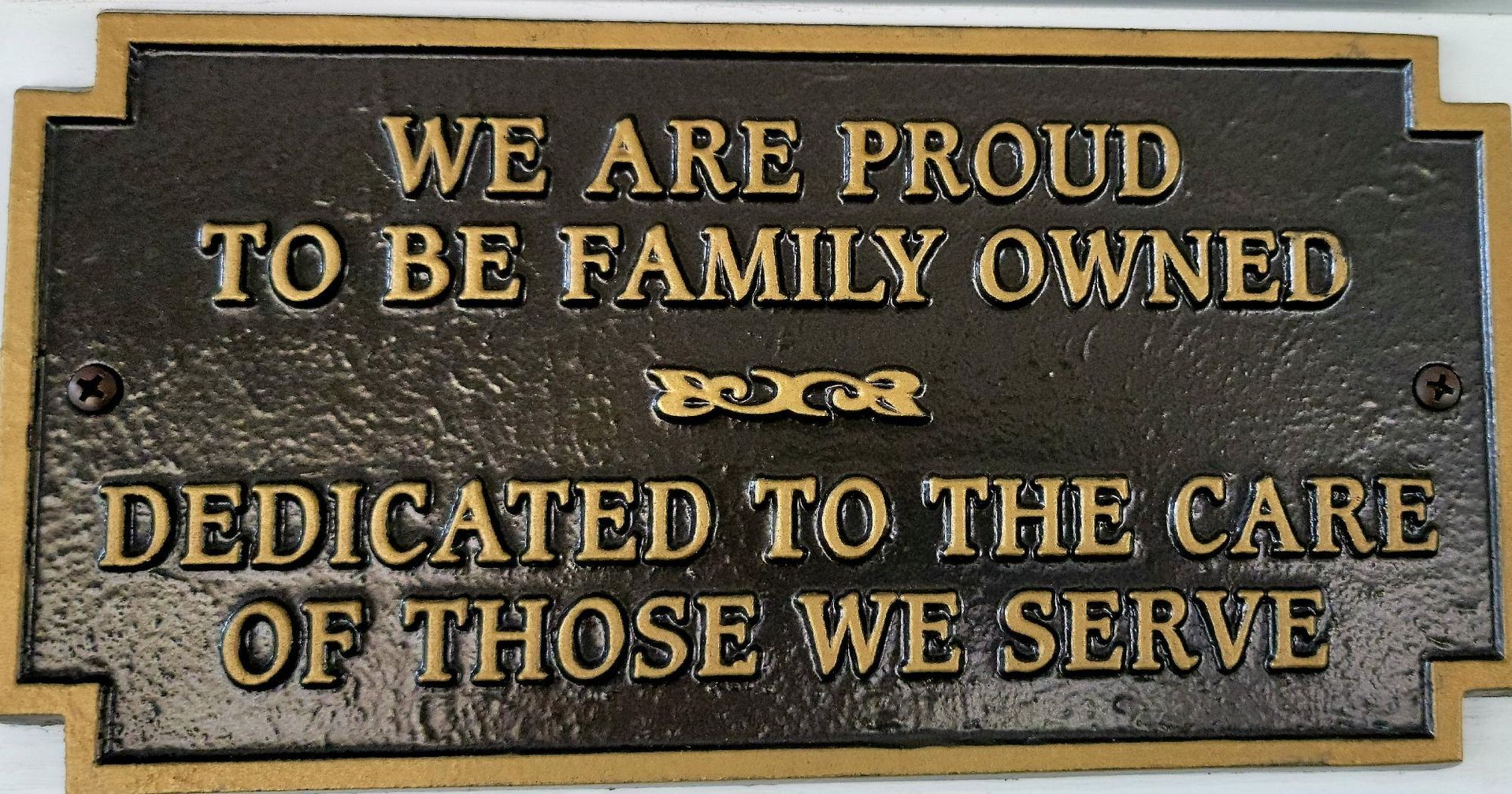 Gold-lettered plaque reading “We are proud to be family owned” and “Dedicated to the care of those we serve.”