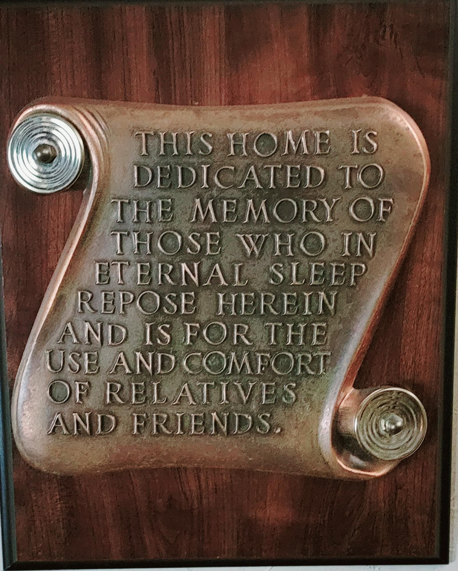 Bronze memorial plaque on wood reading “This home is dedicated to the memory...”