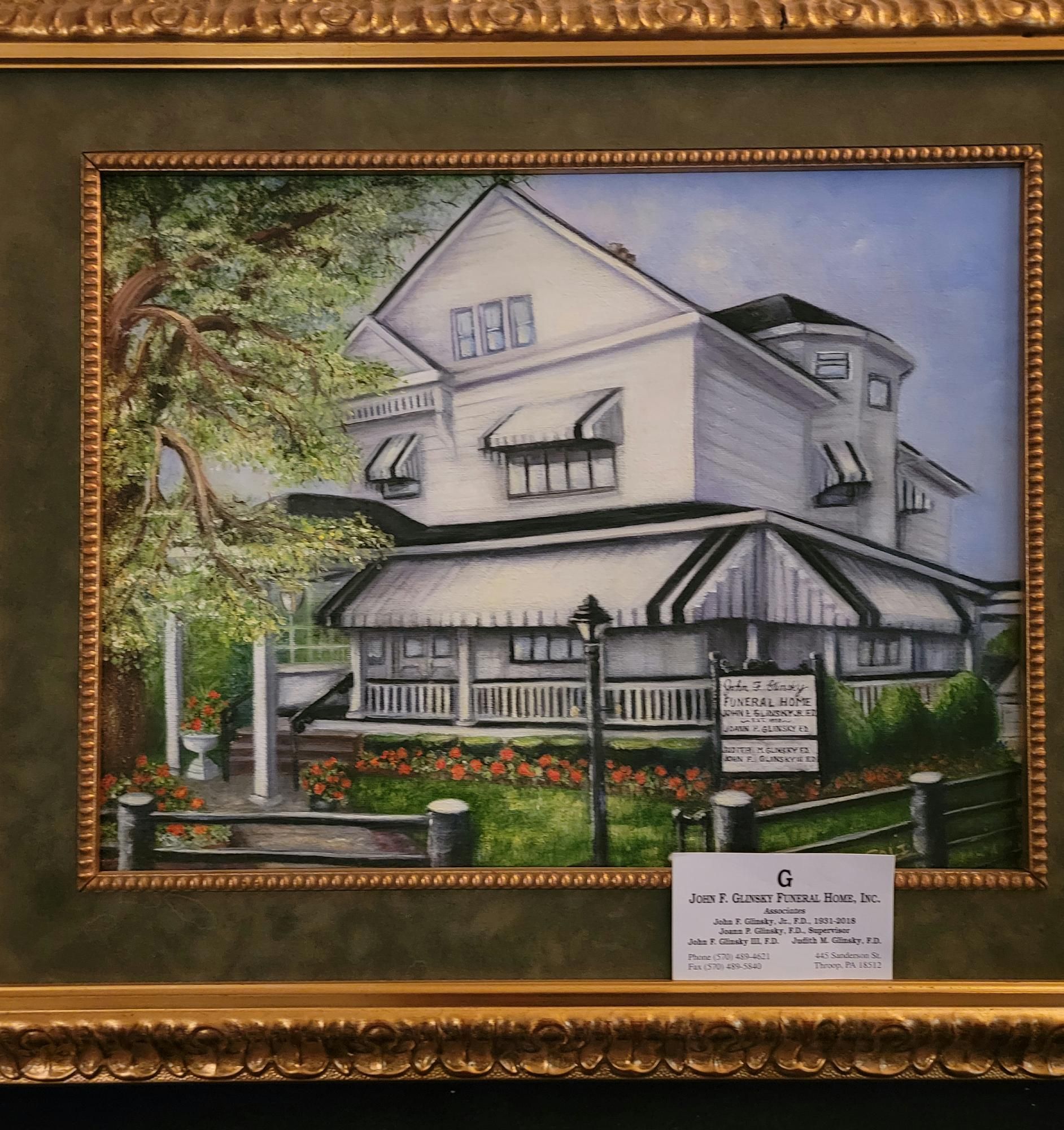Framed painting of a white house with porch, trees, and flowers in a gold frame