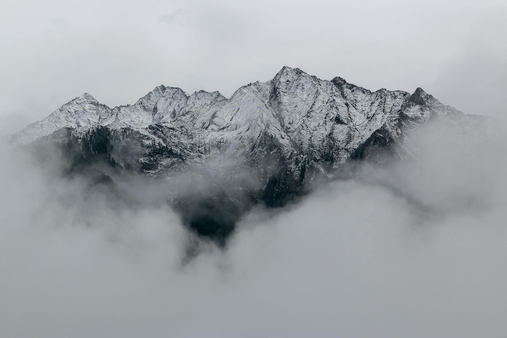 Snow-covered mountain peaks emerge from dense, low-lying clouds under a gray sky.