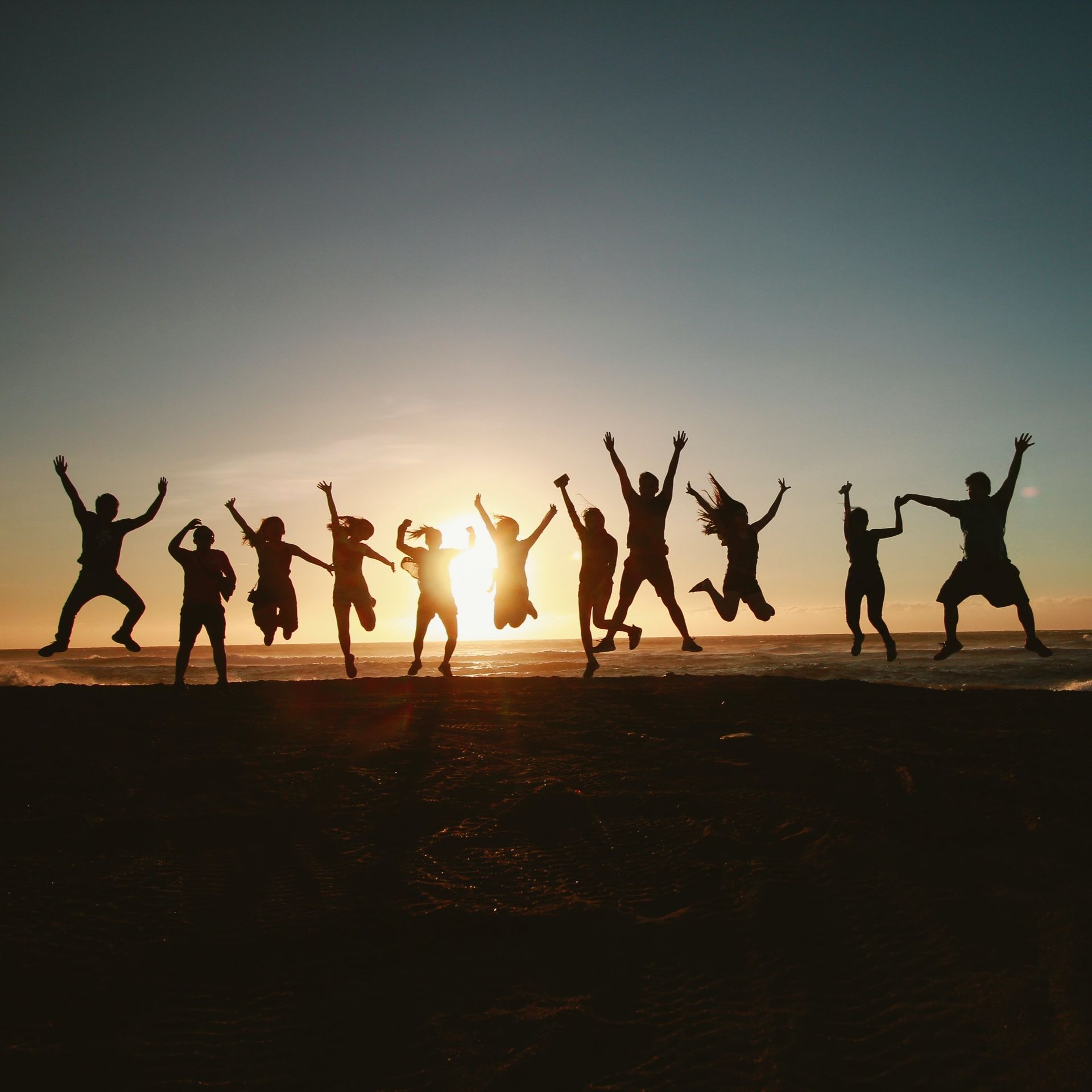 Silhouetted people jumping on a beach at sunset, arms raised in the air.