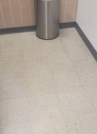 A stainless steel trash can is sitting on a tiled floor in a bathroom.