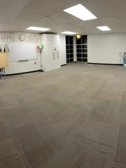 A large empty room with a carpeted floor and a white board on the wall.