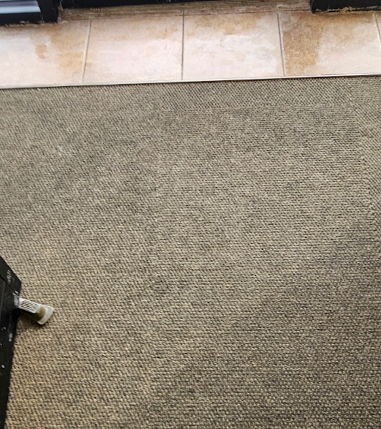 A close up of a carpet on a tiled floor.