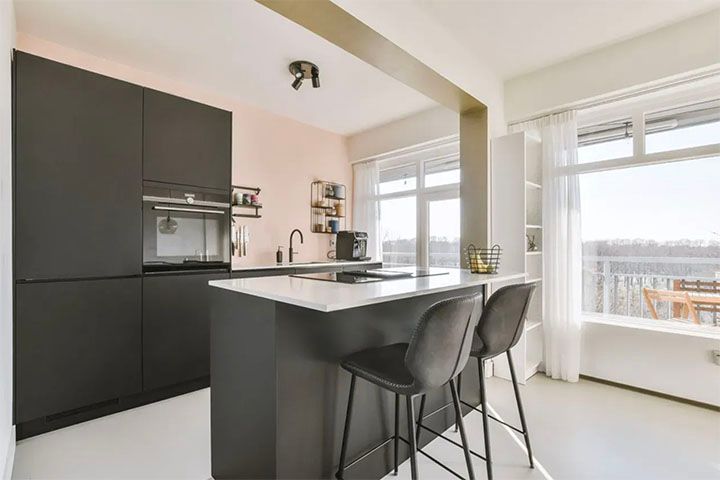 A kitchen with a large island and stools and a large window.