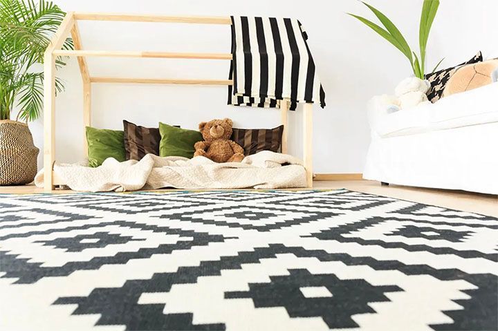 A teddy bear is sitting on a bed in a living room next to a rug.