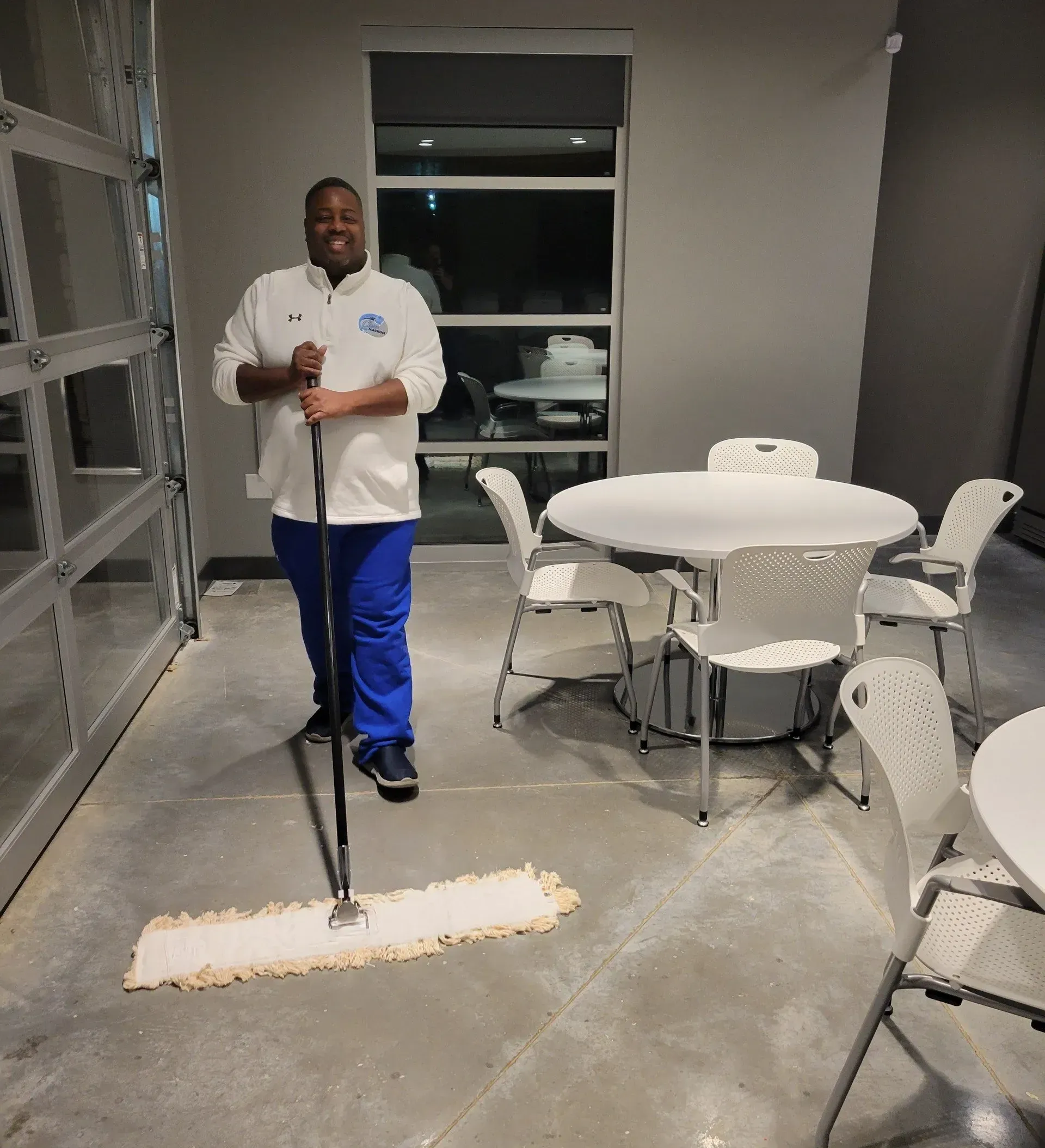 A man is mopping the floor in a room with tables and chairs