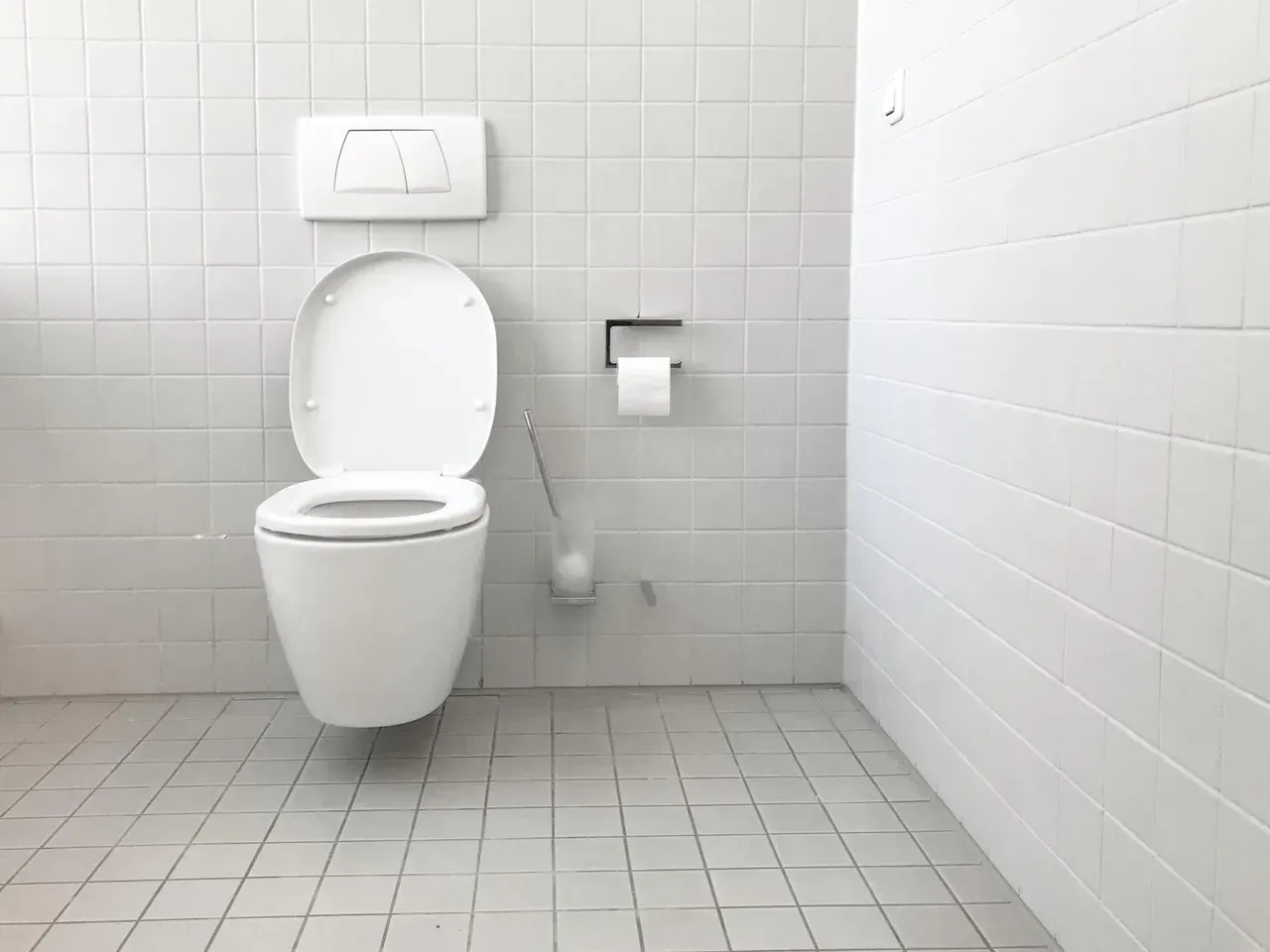 A white toilet is sitting in a bathroom with white tiles.